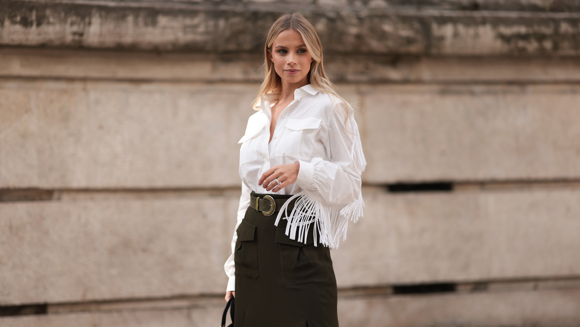 A Fashion Week guest is seen wearing a white shirt with fringes along the sleeves, tucked into an olive midi skirt with pockets at the front, paired with an olive suede belt featuring a round buckle, a silver structured ring, and the rectangular “Lady Dior“ bag in black quilted leather with gold details from Dior before the Elie Saab Womenswear Spring/Summer 2025 Show as part of Paris Fashion Week on September 28, 2024 in Paris, France