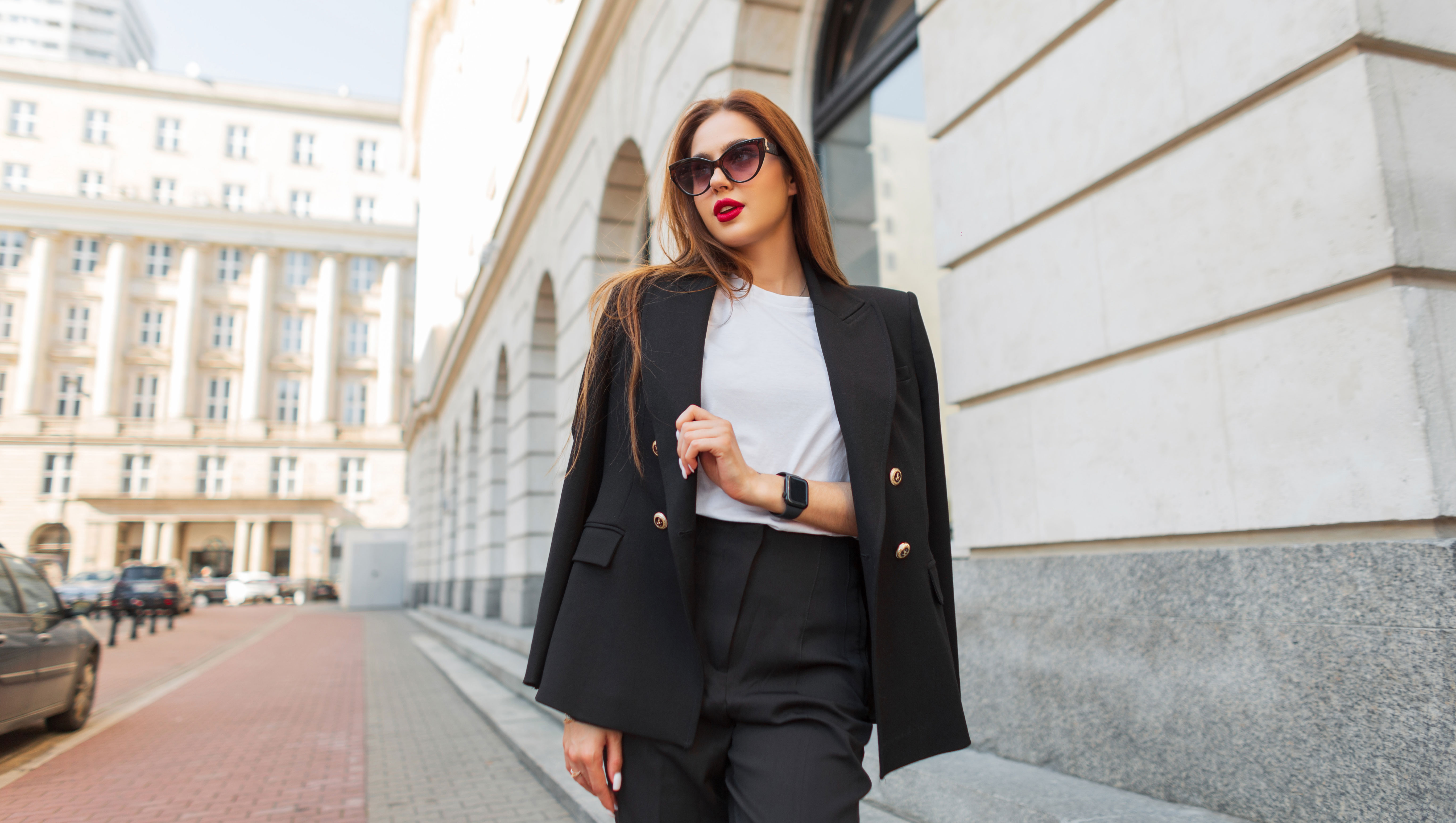 Beautiful urban fashion woman in a stylish black casual suit with vintage sunglasses walks in the city. Pretty business lady