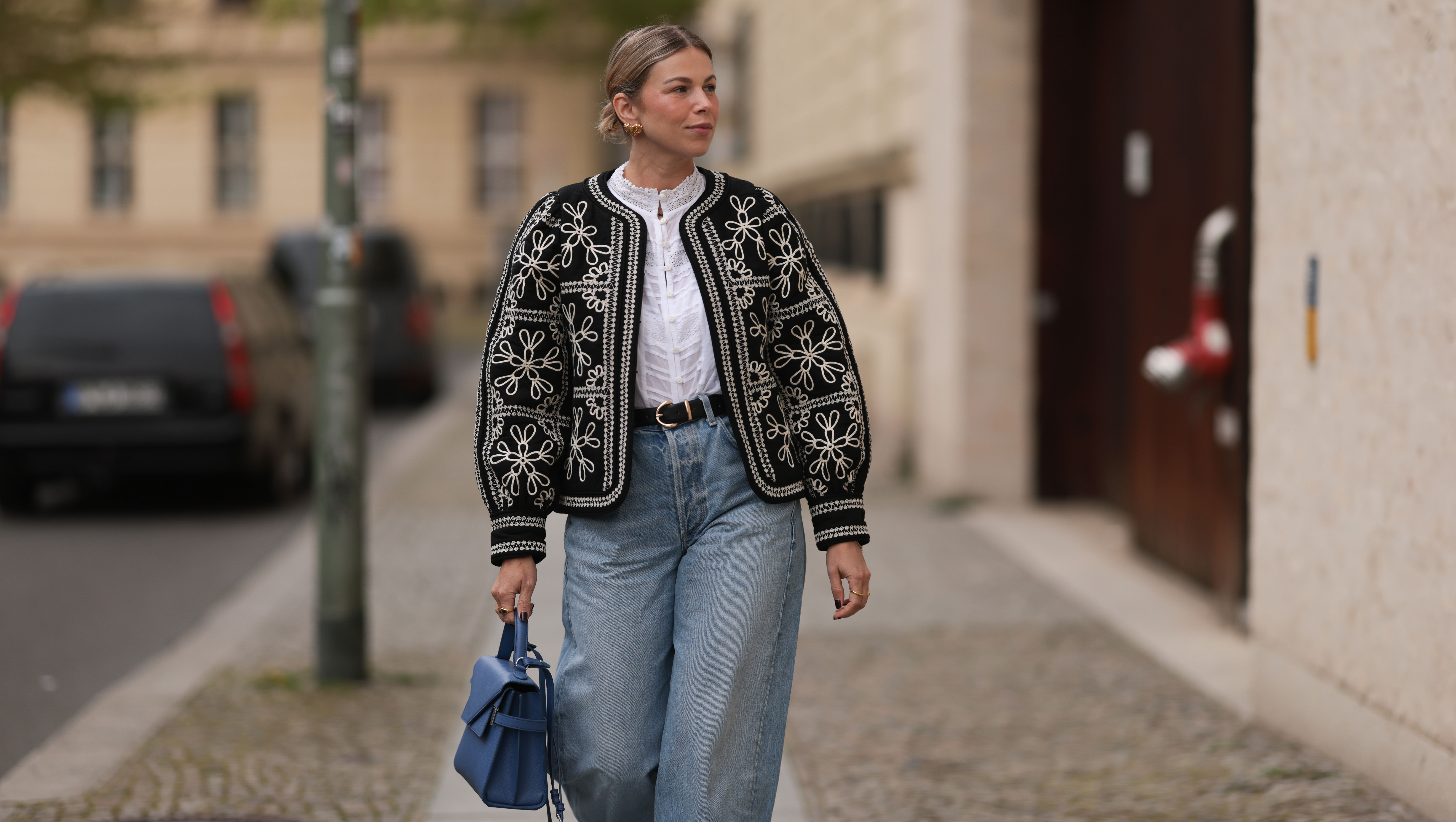 BERLIN, GERMANY - APRIL 08: Aline Kaplan seen wearing gold heart shaped earrings, Sézane black / white flower embroidered jacket, Mango white cotton blouse, Citizen Of Humanity blue denim wide leg jeans, Le Tanneur blue leather bag, on April 08, 2024 in Berlin, Germany.