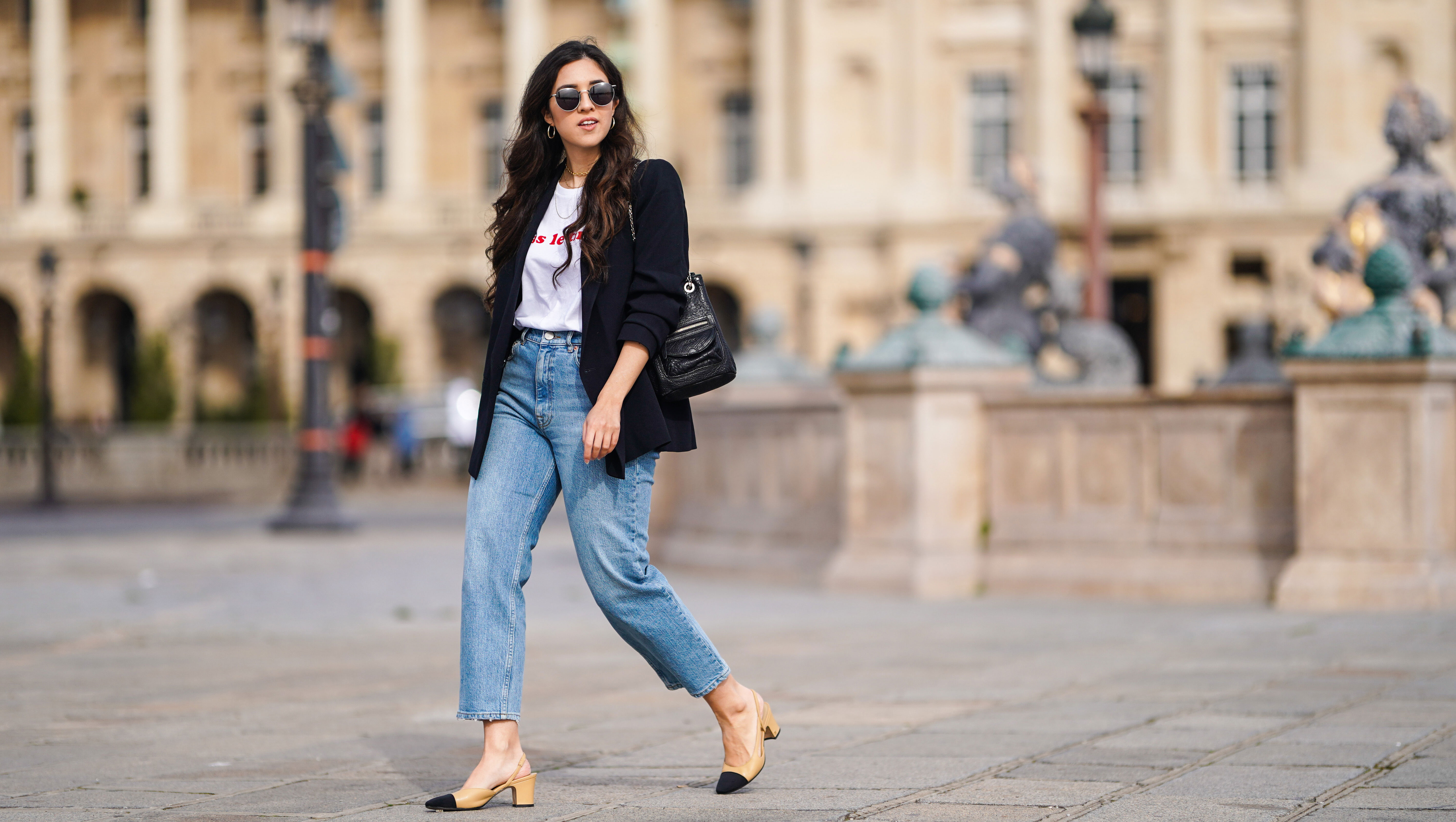 PARIS, FRANCE - FEBRUARY 25: Camille Grandguillote wears sunglasses, a black blazer jacket from Sezane, a black leather bag from Kate Lee, a white t-shirt from "Pas le Time", blue denim jeans pants from Asos, Chanel beige and black slingback shoes, on February 25, 2021 in Paris, France. (Photo by Edward Berthelot/Getty Images)