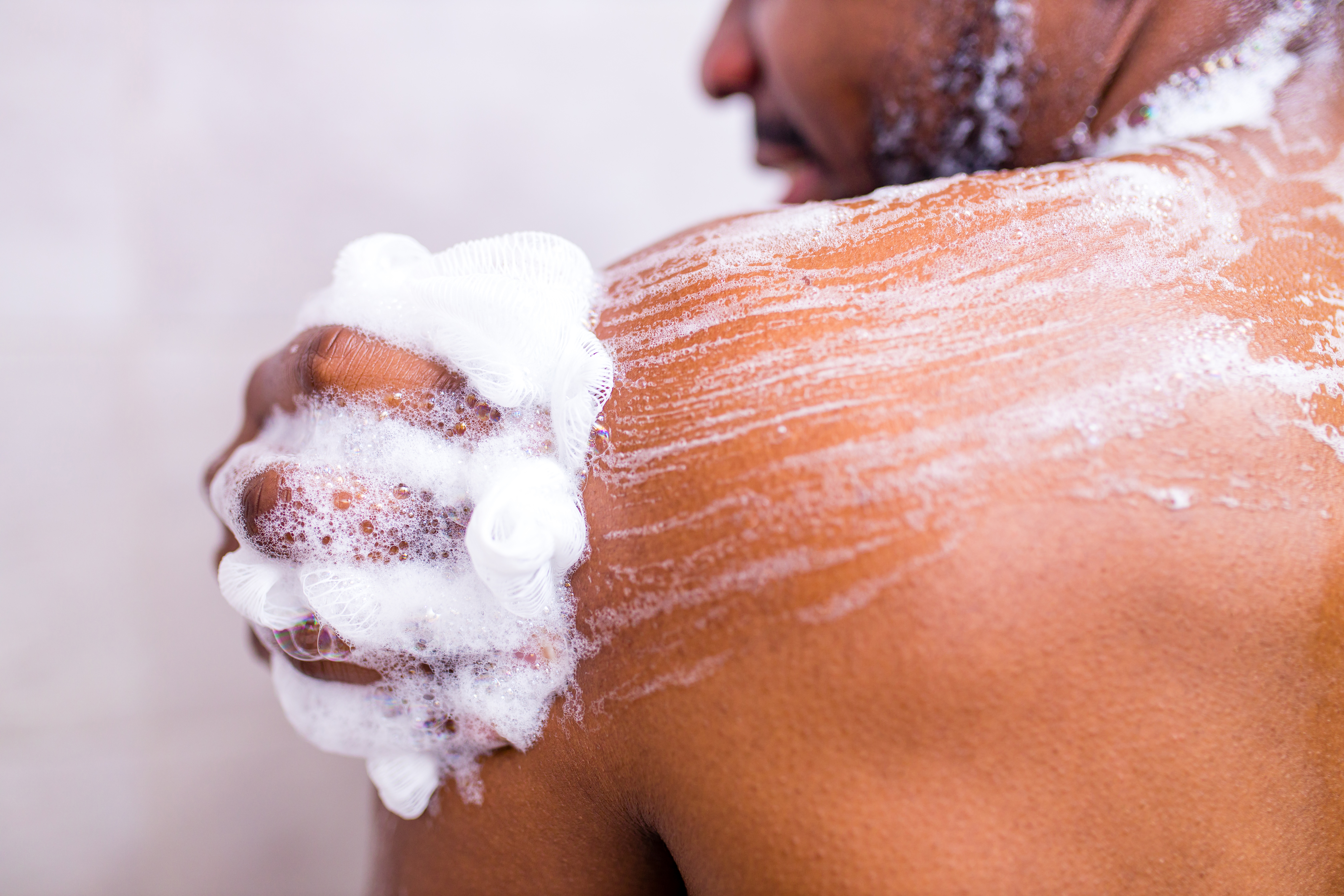 Brazilian man washing body with shower sponge in white bathroom