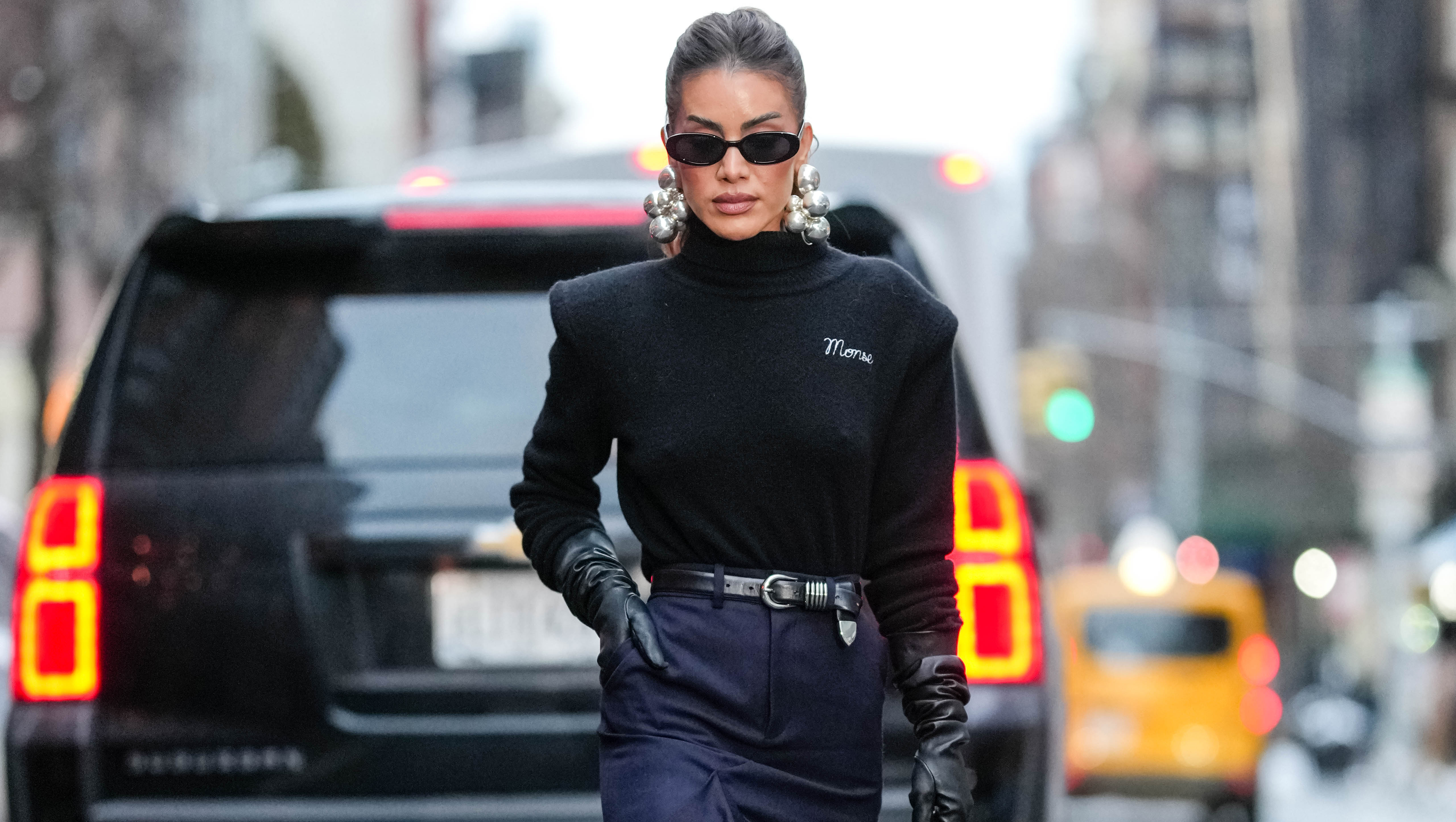 NEW YORK, NEW YORK - FEBRUARY 09: Camila Coelho wears black sunglasses, silver earrings, black turtle long sleeve sweater, shiny black leather gloves, shiny black leather belt, black high waisted high slit midi skirt, shiny black pointed toe knee high leather boots, shiny black alaïa leather bag, outside Monse, during the New York Fashion week Fall/Winter 2025 on February 9, 2025 in New York, New York. (Photo by Edward Berthelot/Getty Images)