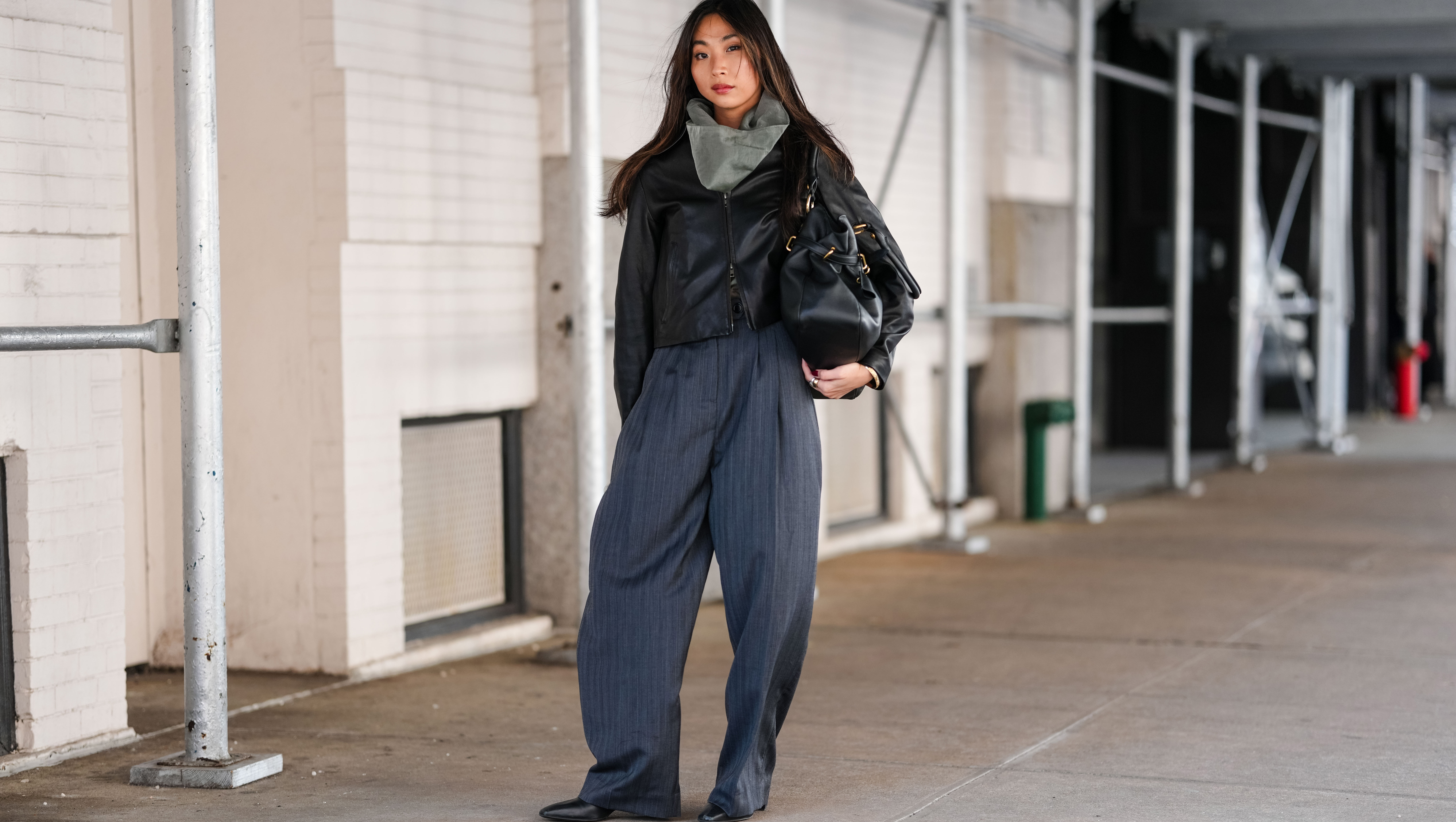 NEW YORK, NEW YORK - FEBRUARY 07: A guest wears dark gray scarf, shiny black cropped leather jacket, shiny black leather bag, dark gray pinstripe high waisted loose trouser pants, shiny black pointed toe heeled boots leather shoes, outside Theory, during the New York Fashion week Fall/Winter 2025 on February 7, 2025 in New York, New York. (Photo by Edward Berthelot/Getty Images)