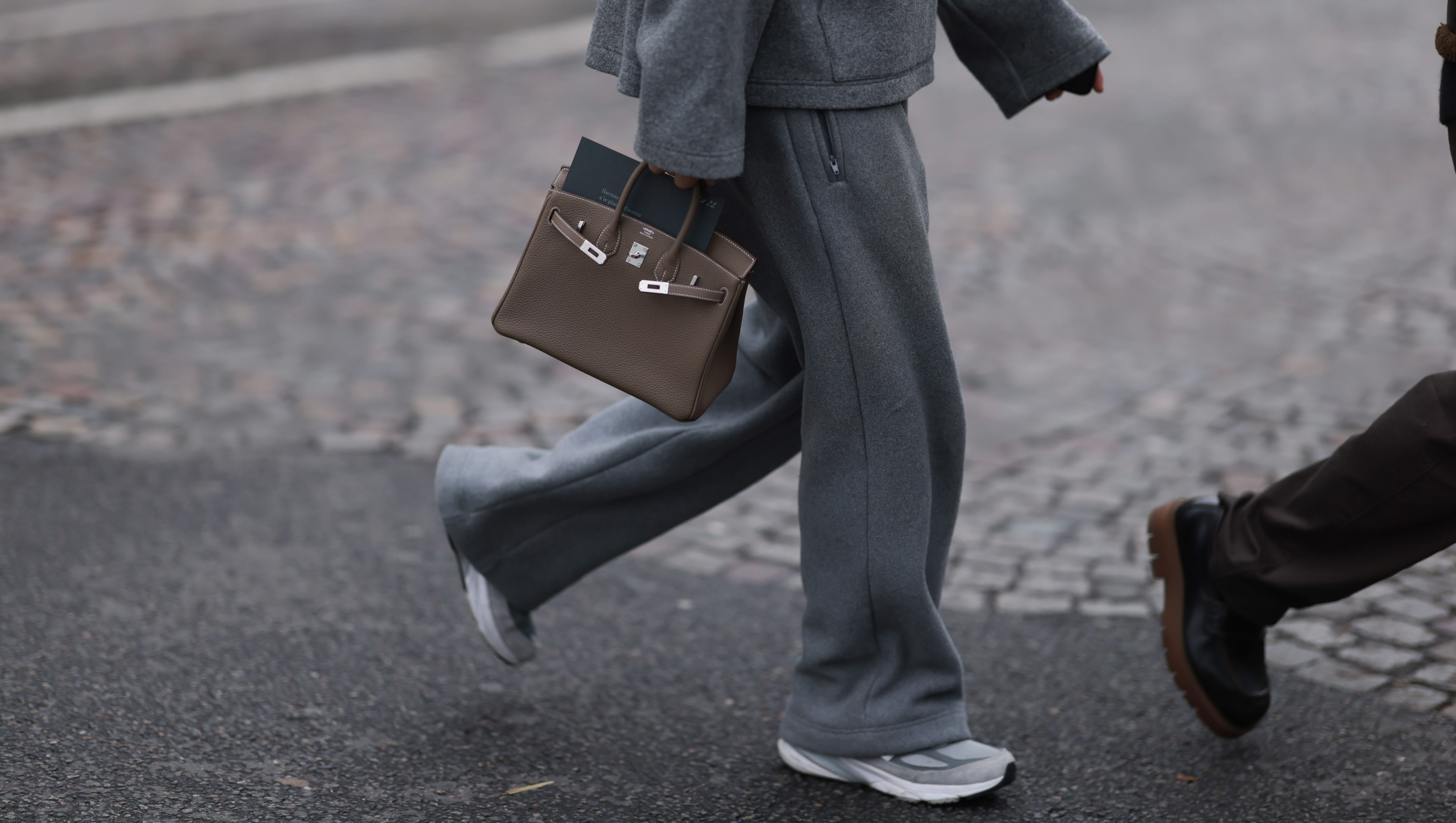 PARIS, FRANCE - JANUARY 25: Fashion Week Guest seen wearing a grey jogging suit, jacket, wide jogging pants and sport sneaker, Hermes taupe Birkin bag outside Hermes Show, during the Menswear Fall Winter 2025/2026 as part of Paris Fashion Week on January 25, 2025 in Paris, France. (Photo by Jeremy Moeller/Getty Images)