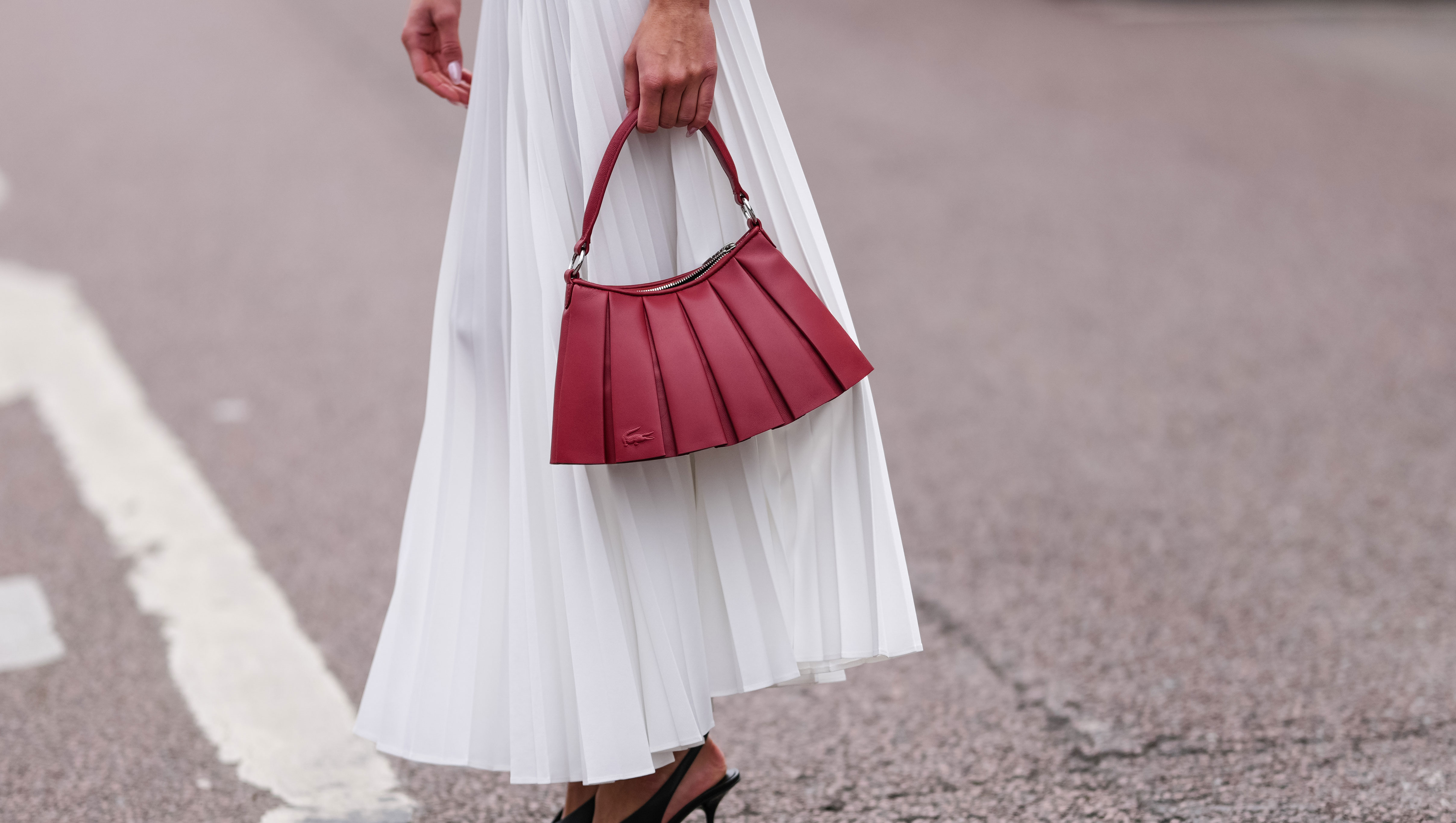 PARIS, FRANCE - MARCH 09: Amalie Bladt wears white pleated Lacoste midi skirt, a gold bracelet, a gold watch, shiny dark red Lacoste leather bag, outside Lacoste, during the Paris Fashion week Women's Fall/Winter 2025-2026 on March 9, 2025 in Paris, France. (Photo by Edward Berthelot/Getty Images)