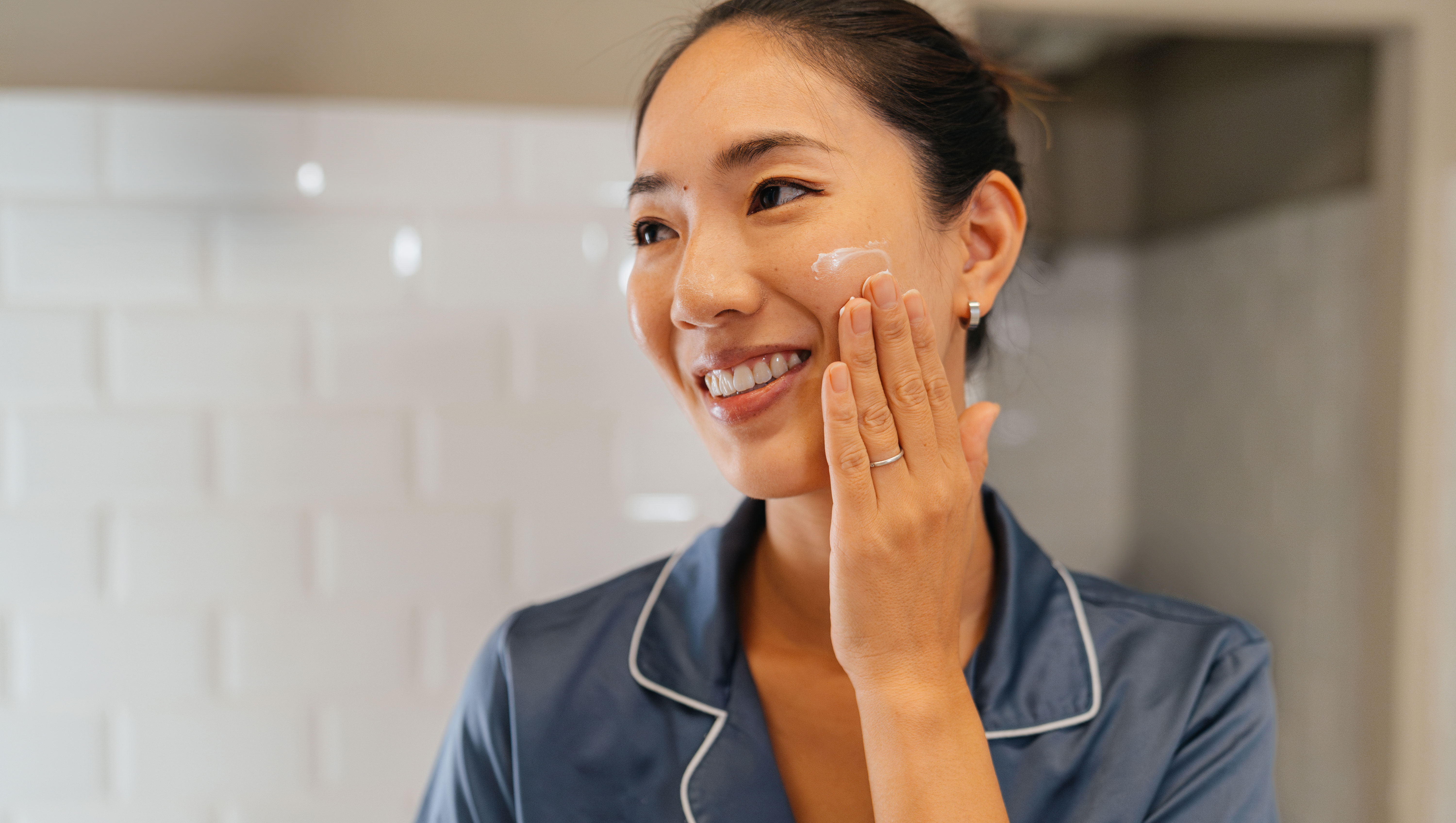 Japanese woman looking her skin in the mirror, applying facial creme and preparing her self before going to work in the bathroom