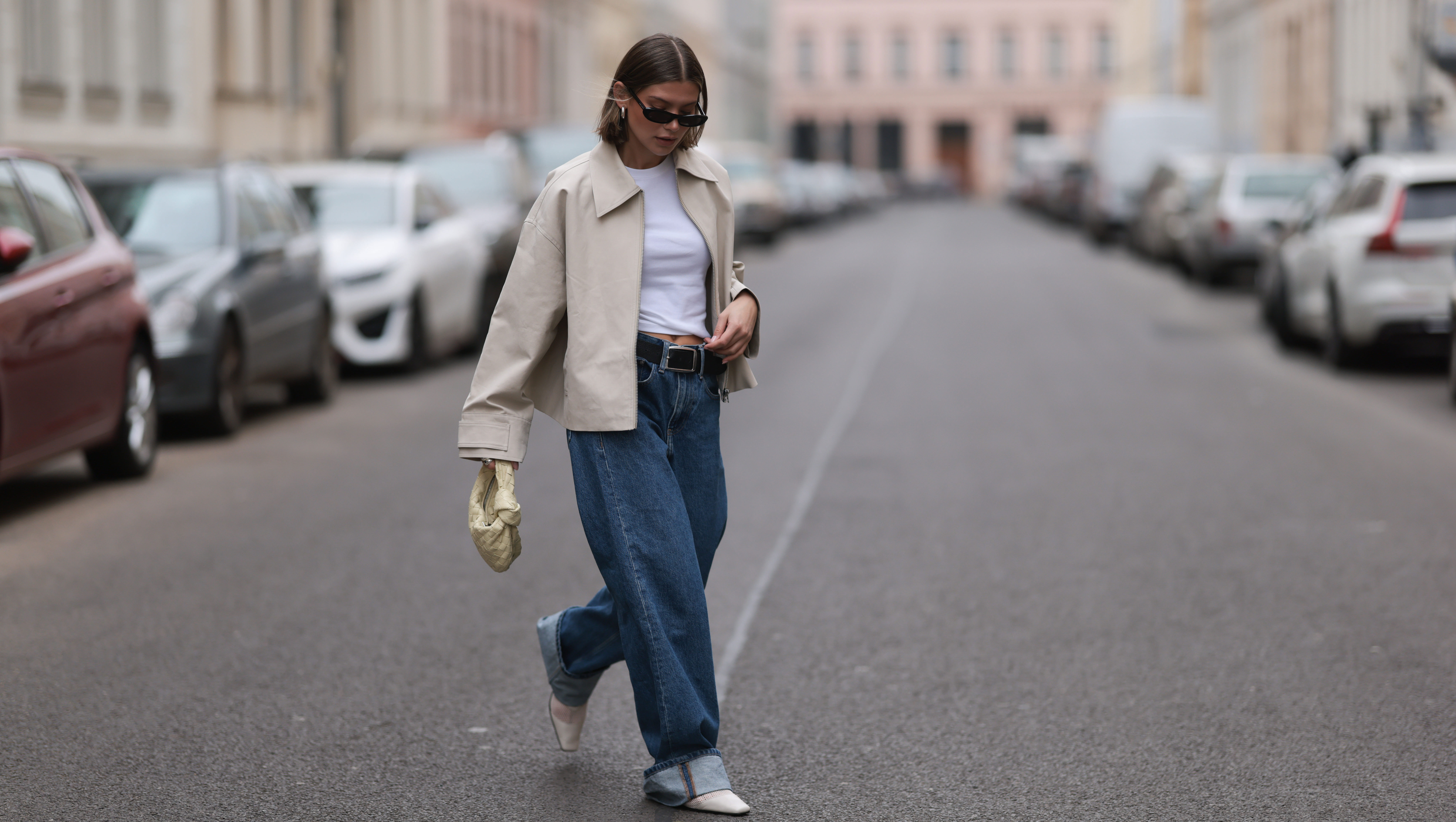 BERLIN, GERMANY - APRIL 12: Sophia Geiss seen wearing Saint Lauren black sunglasses, Uniqlo white cotton basic top, Calvin Klein blue denim baggy wide leg jeans pants, black leather belt, Meotine creamy white canvas jacket, Bottega Veneta creamy white / vanilla leather mini Jodie bag and Vagabond white leather mesh ballerinas, on April 12, 2024 in Berlin, Germany.