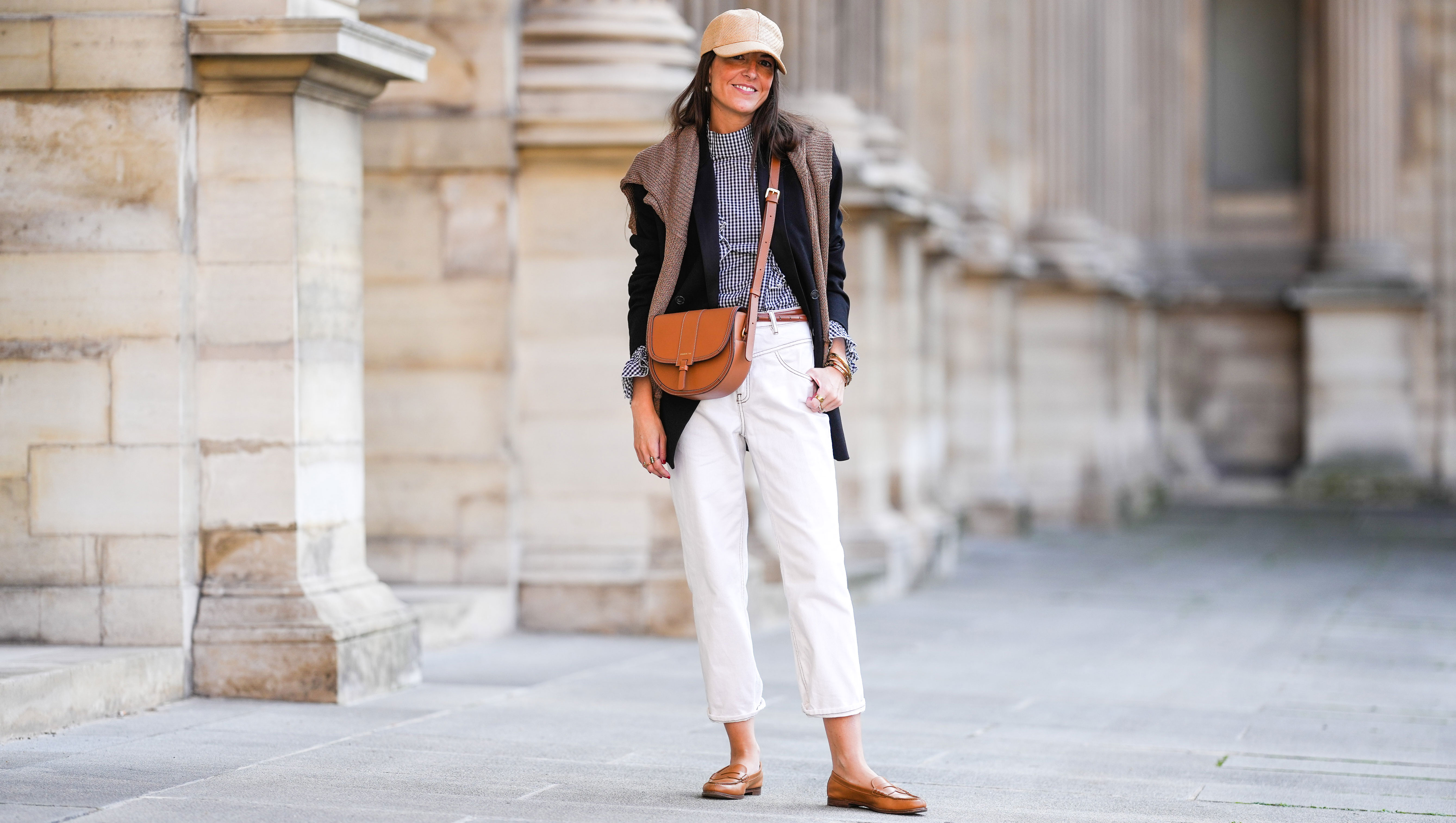 PARIS, FRANCE - OCTOBER 10: Alba Garavito Torre wears a wicker cap, a gingham black and white shirt with Long Sleeve Ruffles from Serendipia, Mom jeans in white by Maison 123 Paris, an oversized black blazer jacket by Munthe, caramel loafers shoes by Church’s, a caramel leather crossbody bag Windsor Paris64, a beige wool sweater over the shoulders, on October 10, 2021 in Paris, France. (Photo by Edward Berthelot/Getty Images)