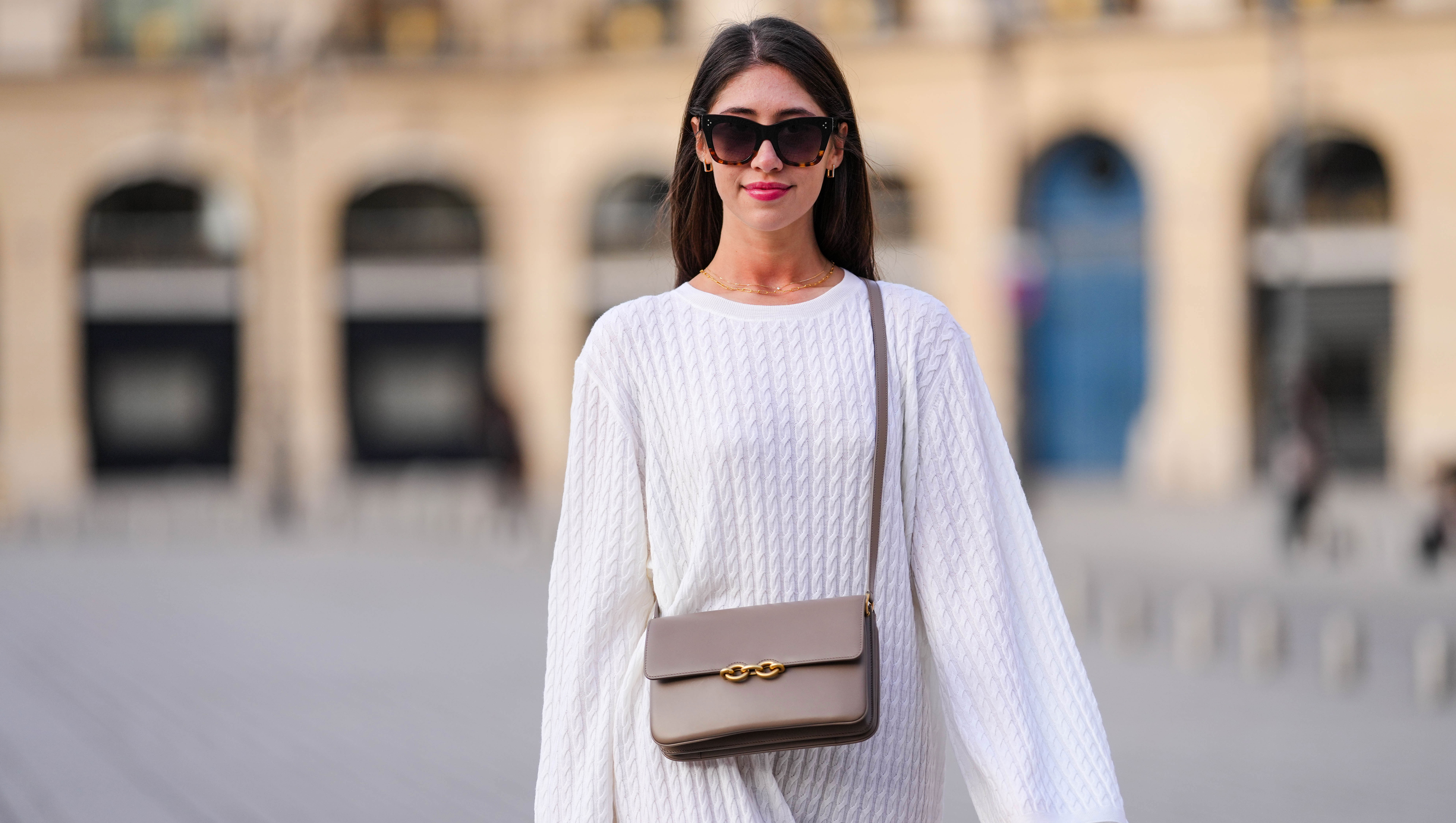 PARIS, FRANCE - APRIL 17: Bianca Derhy wears black sunglasses from Celine, gold and rhinestones earrings, gold chain necklaces, a white embossed braided wool pattern oversized long sleeves / midi dress, a gray brown matte leather crossbody bag with gold chain buckle, a gold ring, during a street style fashion photo session, on April 17, 2022 in Paris, France. (Photo by Edward Berthelot/Getty Images)