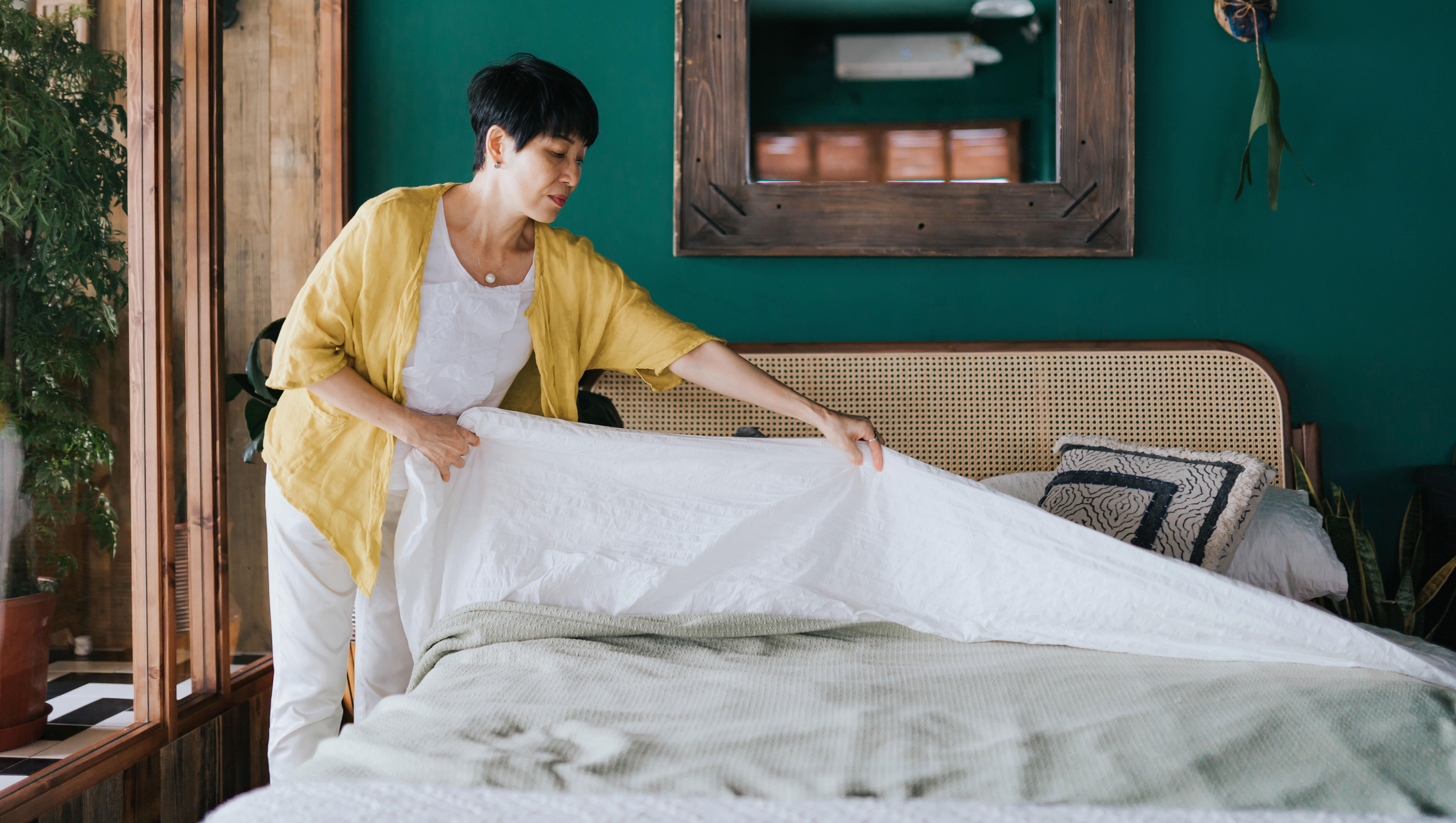 Senior Asian woman doing her morning routine, making up her bed at home. Let's get the day started - stock photo