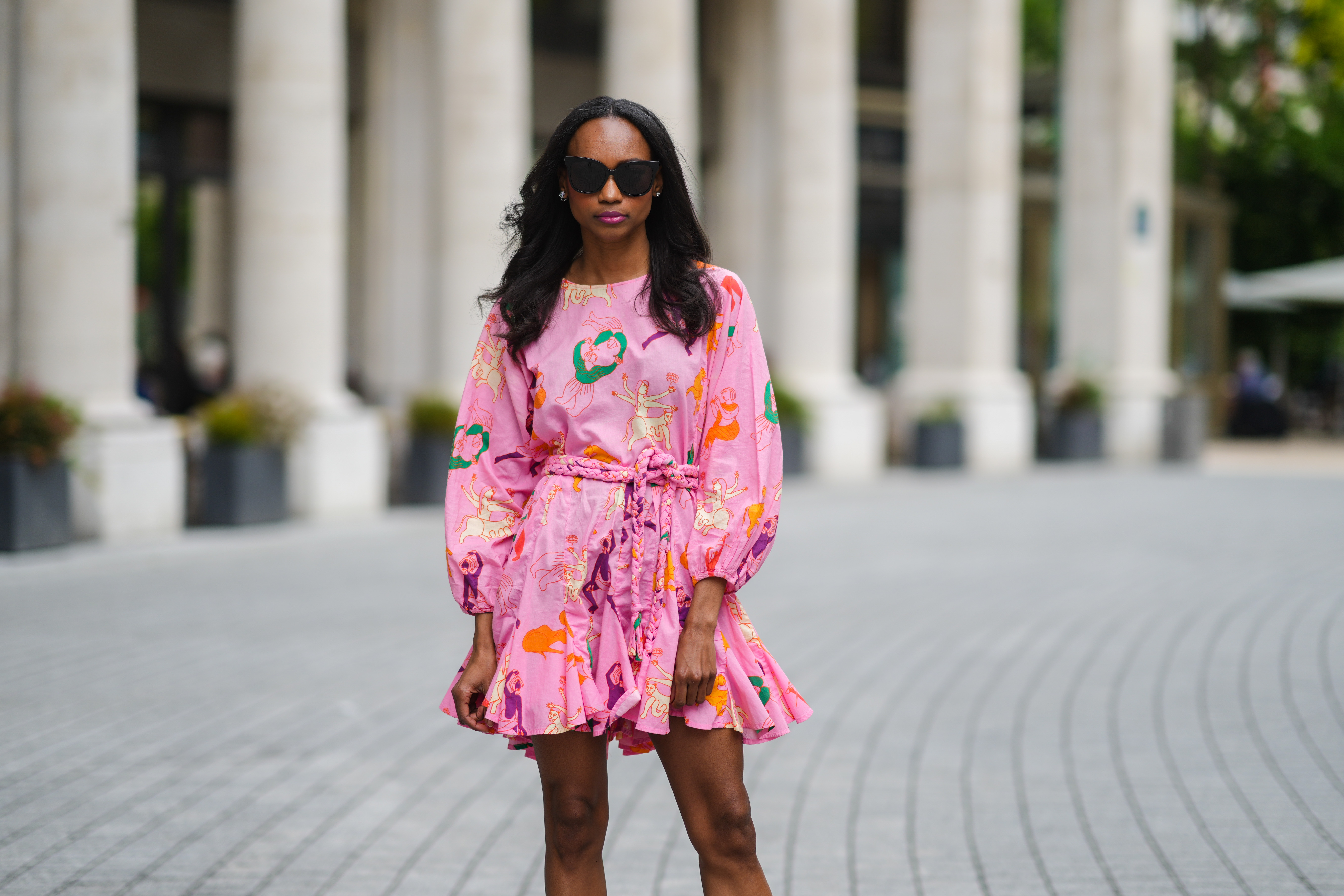 Emilie Joseph @in_fashionwetrust wears sunglasses, silver earrings, a Rhode printed summer vacay Ella dress in vibrant pink with long dolman sleeves with elastic cuffs and a full a flirty hem and a waist-cinching braided belt, on May 27, 2021 in Paris, France.