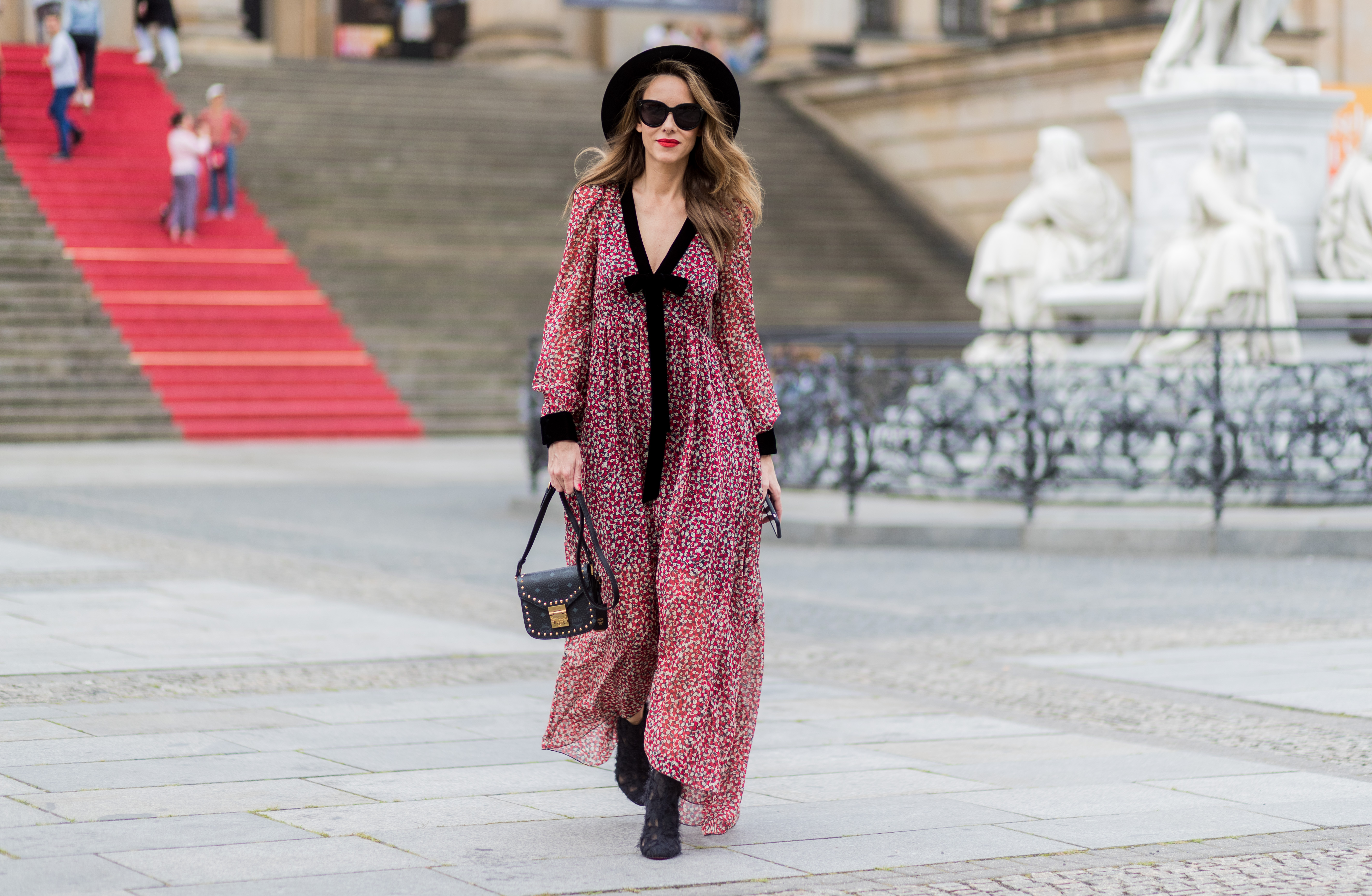 Alexandra Lapp wearing Boho Style, a red and cream floral print maxi dress from Philosophy di Lorenzo Serafini in sheer silk chiffon and bold black trims with a ribbon tie, Toubootfrou ankle boots with rete, organze and suede in black from Christian Louboutin, Celine Audrey sunglasses in black, Maison Maison Michel hat Virginie fedora, MCM Patricia Shoulder Bag in a vintage shape during the Mercedes-Benz Fashion Week Berlin Spring/Summer 2018 on July 7, 2017 in Berlin, Germany.