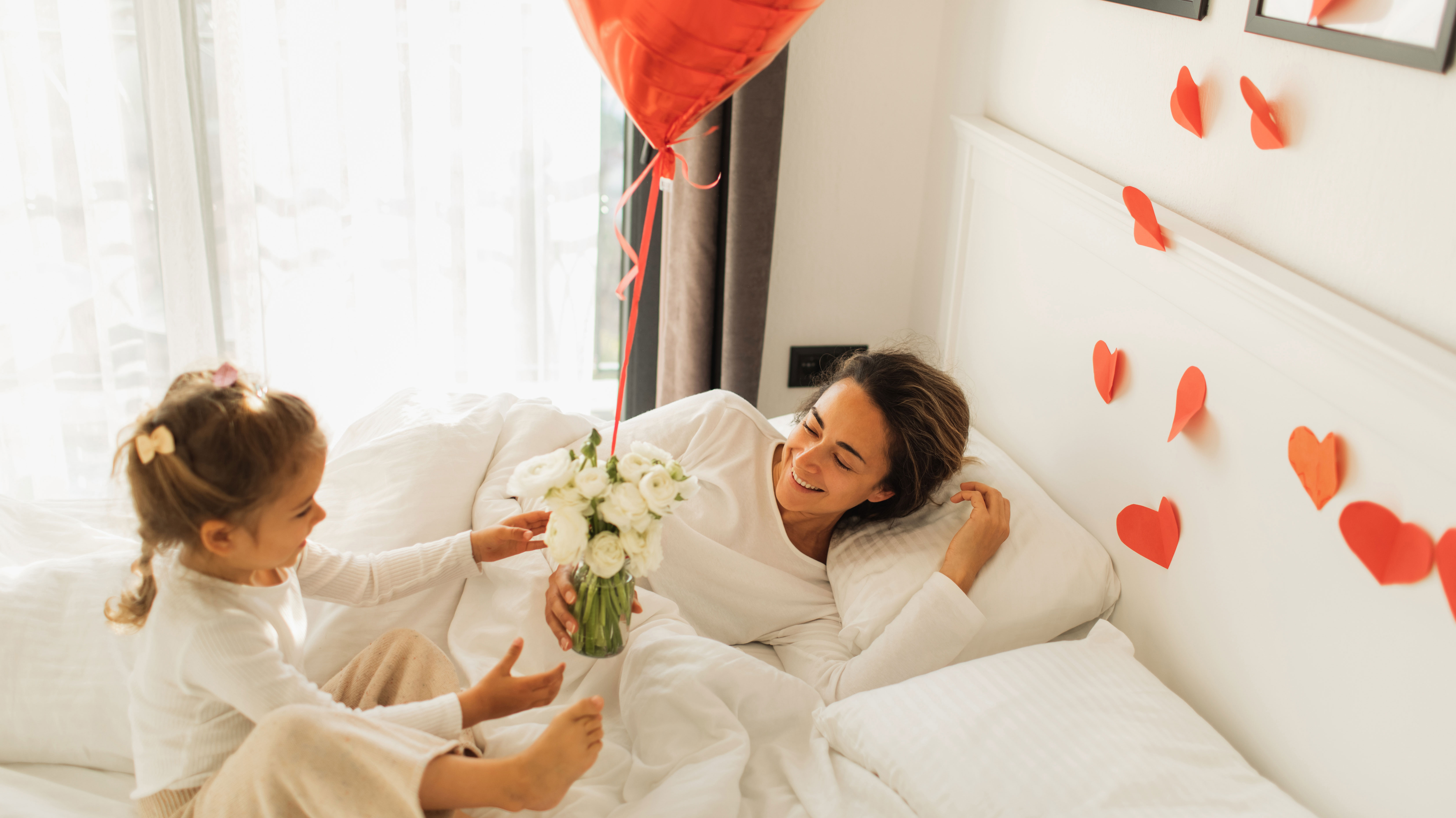 Little Daughter wakes up mother and Giving Gifts for her in Bed. - stock photo