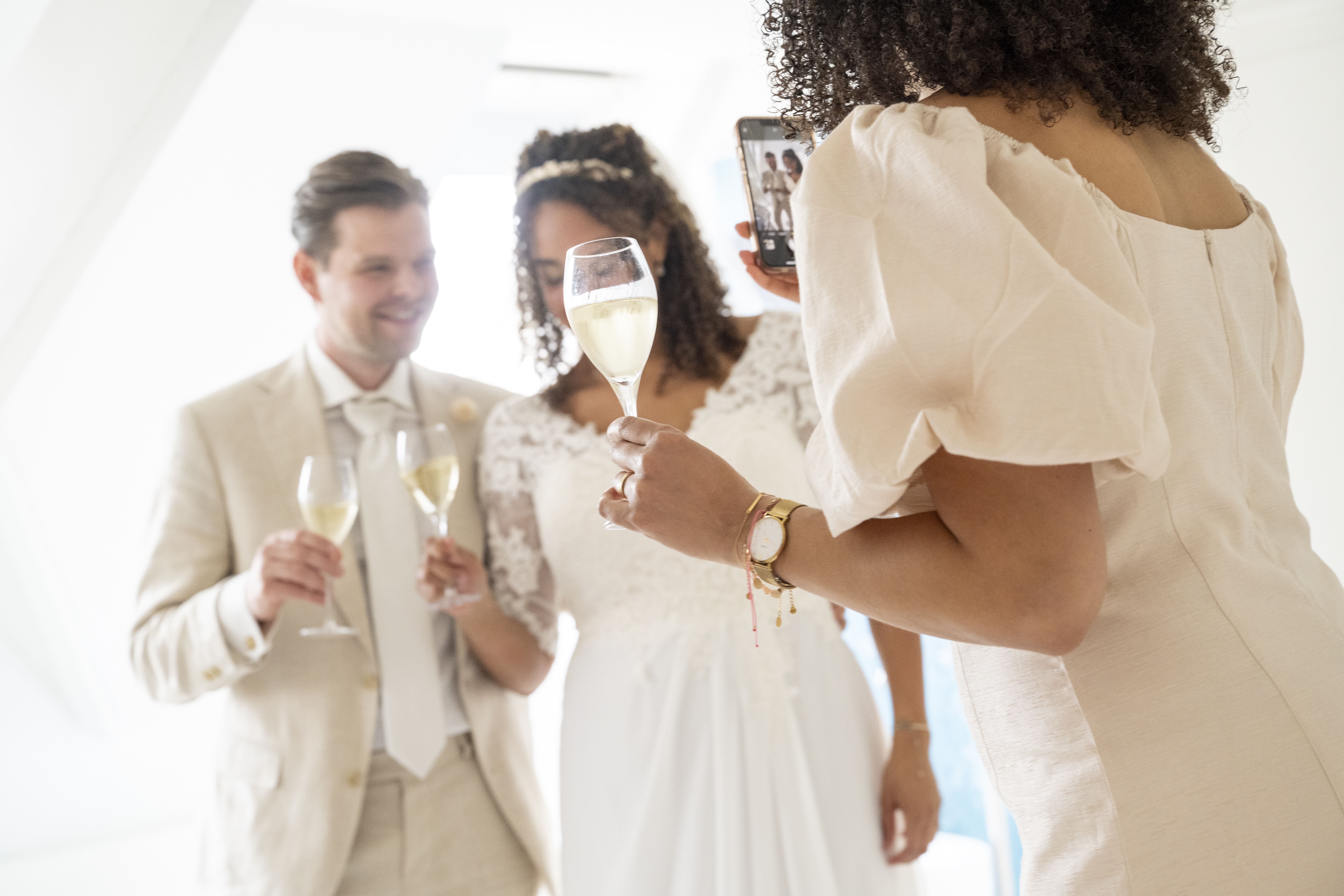 Bride and groom holding champagne glasses with a guest at a wedding celebration, sharing a toast