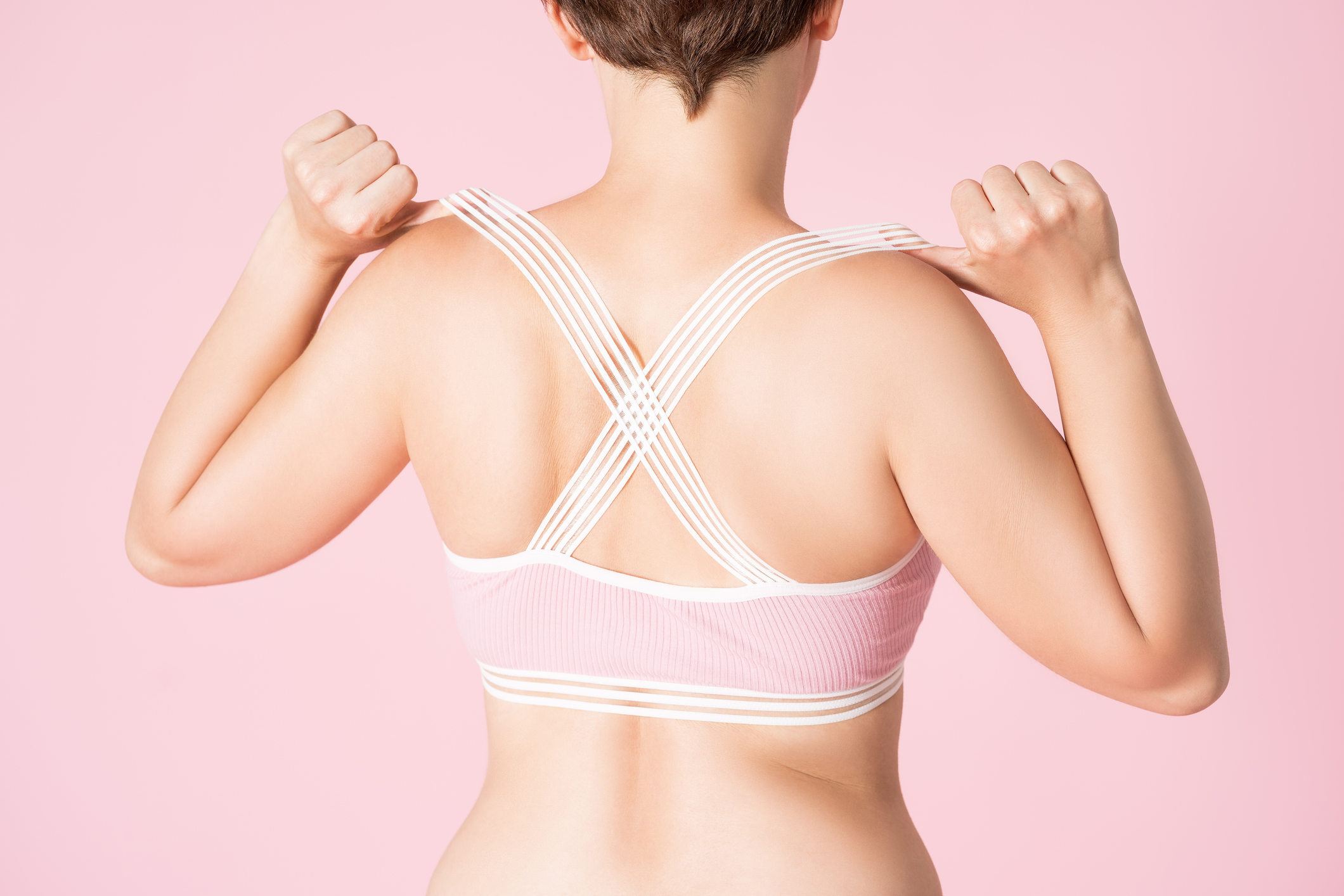 Fit woman in sports bra on pink background, body care concept