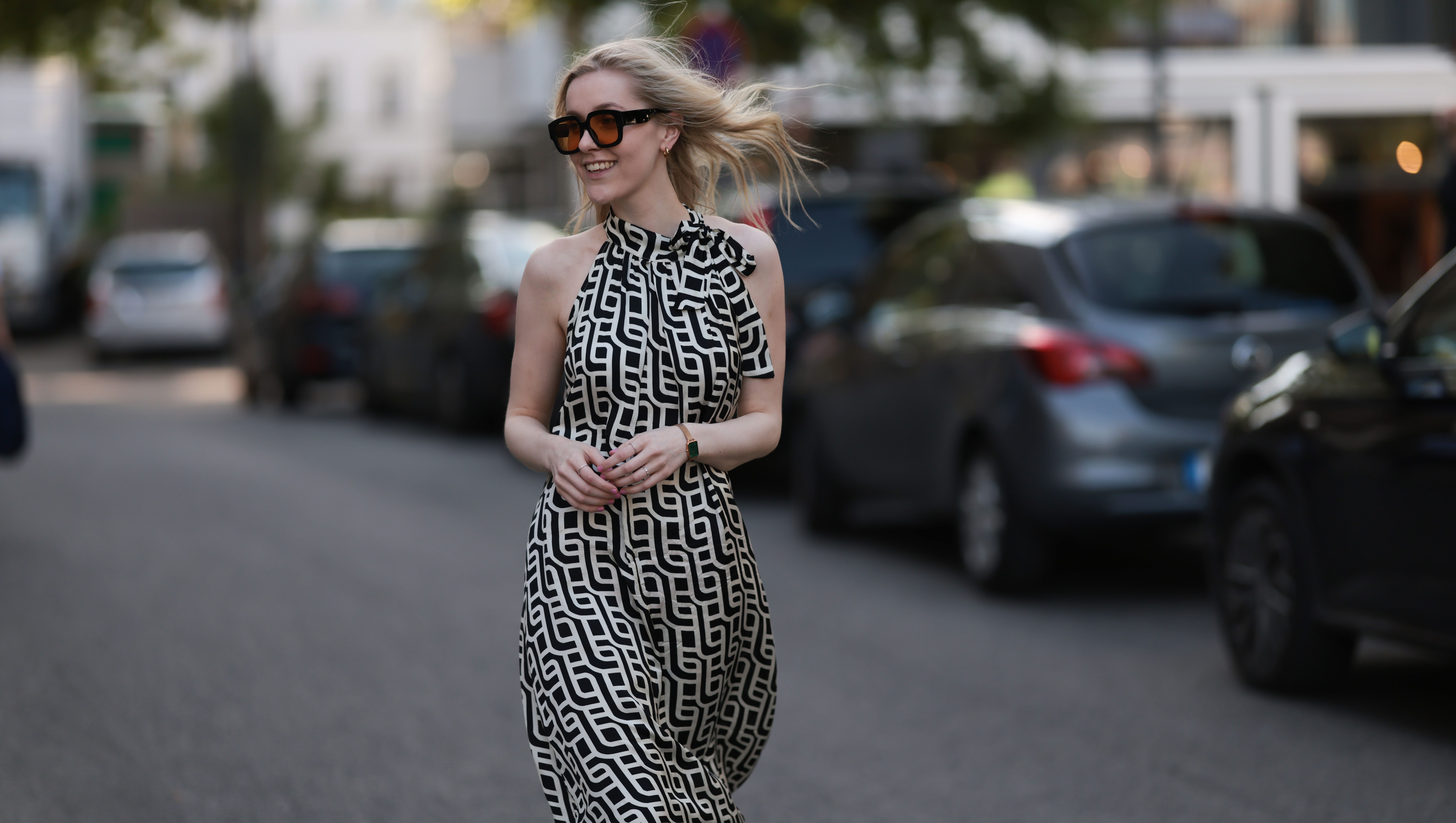 BERLIN, GERMANY - JUNE 19: Lil Paulin is seen wearing oversized black square-framed sunglasses with orange lenses and wide temples, gold hoop earrings, a flowy sleeveless maxi dress with a halter neck and a geometric black and white pattern, a gold rectangular watch from Daniel Wellington, and several filigree silver rings on June 19, 2025 in Berlin, Germany. (Photo by Jeremy Moeller/Getty Images)