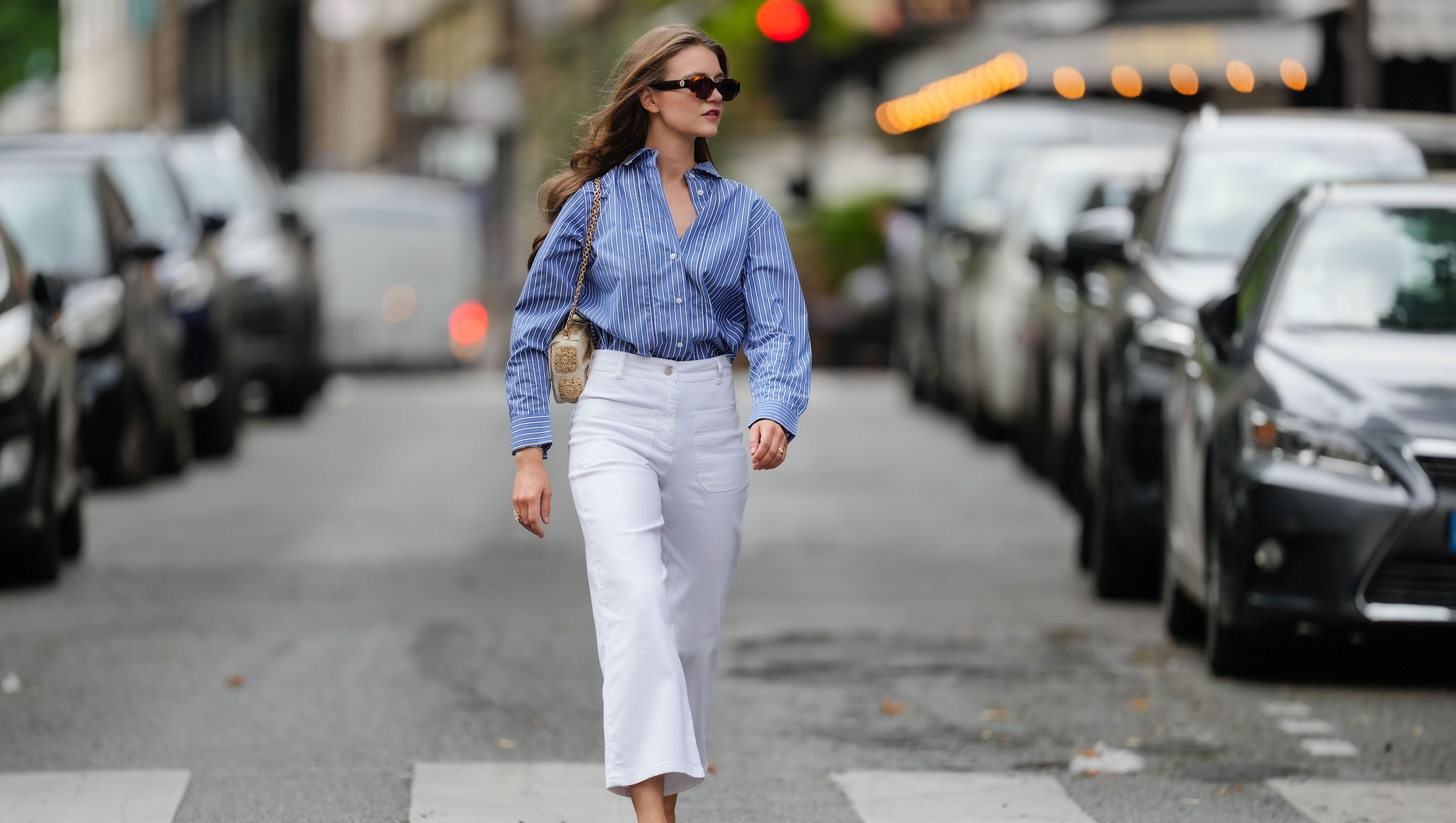 PARIS, FRANCE - MAY 20: Segolene Hyppolite wears sunglasses, a blue and white oversized shirt from Tommy Hilfiger, a raffia beige bag from Vanessa Bruno, high waist white denim pants from Vanessa Bruno, Chanel slingback shoes in blue denim with black tips, during a street style fashion photo session, on May 20, 2024 in Paris, France. (Photo by Edward Berthelot/Getty Images)