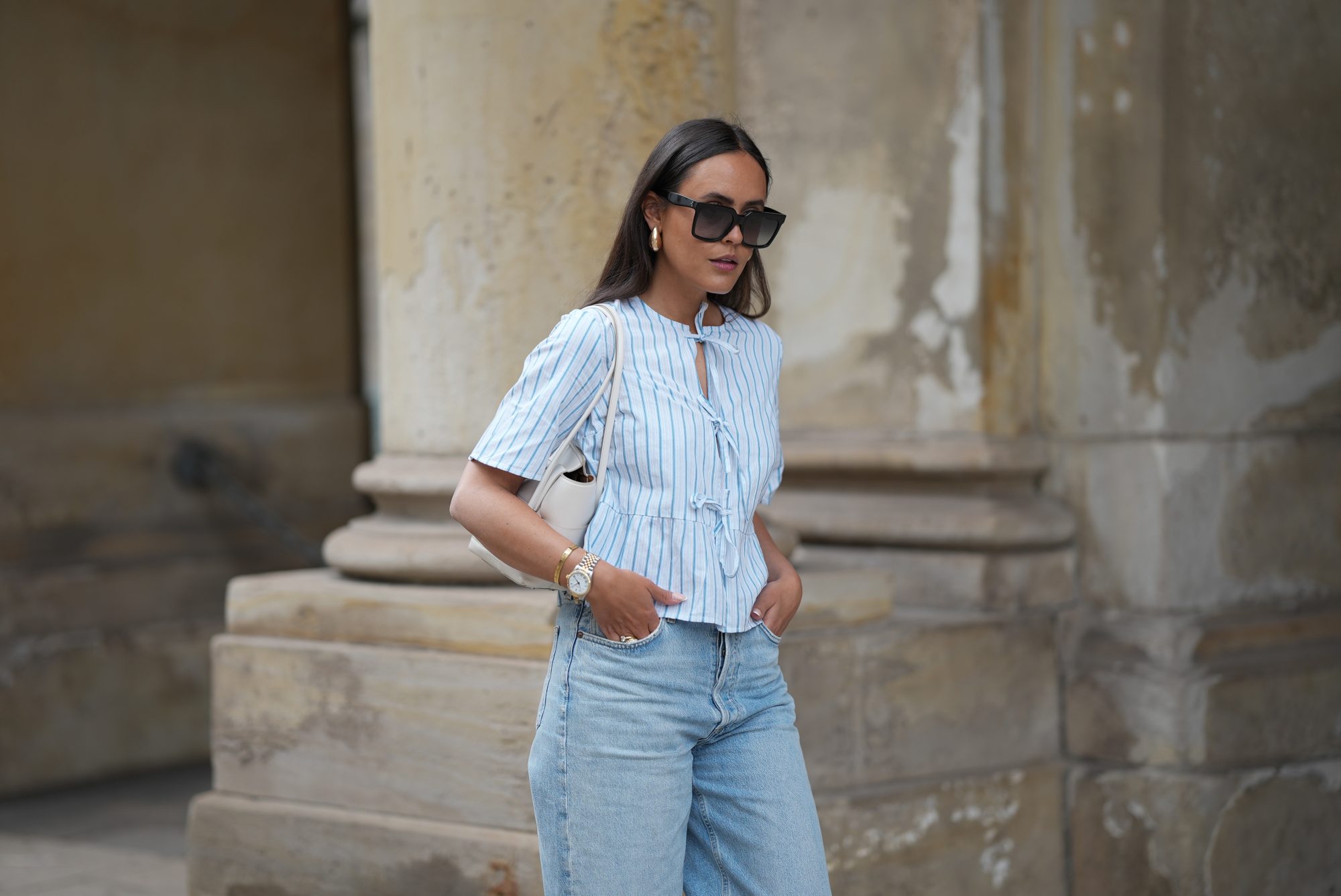 HAMBURG, GERMANY - MAY 7: Laura Noltemeyer is seen wearing a light indigo blue wide leg jeans from Agolde, a cotton puff sleeve blouse with ties in the front in white with blue stripes from Sézane, black oversized cat-eye acetate sunglasses from Celine, Arco handbag in white intrecciato leather from Bottega Veneta, big golden drop-shaped earrings, a small Lady-Datejust watch in gold-silver from Rolex, a golden LOVE bracelet from Cartier, stacked golden rings from Cartier on May 7, 2025 in Hamburg, Germany. (Photo by Moritz Scholz/Getty Images)