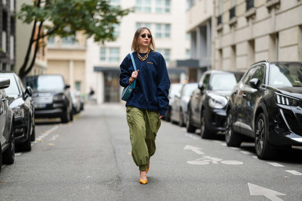PARIS, FRANCE - NOVEMBER 09: Emy Venturini wears black Rayban sunglasses, a dark blue Supreme sweater, a gold Margiela necklace, a light blue leather Liase bag, khaki wide-leg pants, orange leather Roger Vivier high heels, during a street style fashion photo session, on November 09, 2024 in Paris, France. (Photo by Edward Berthelot/Getty Images)