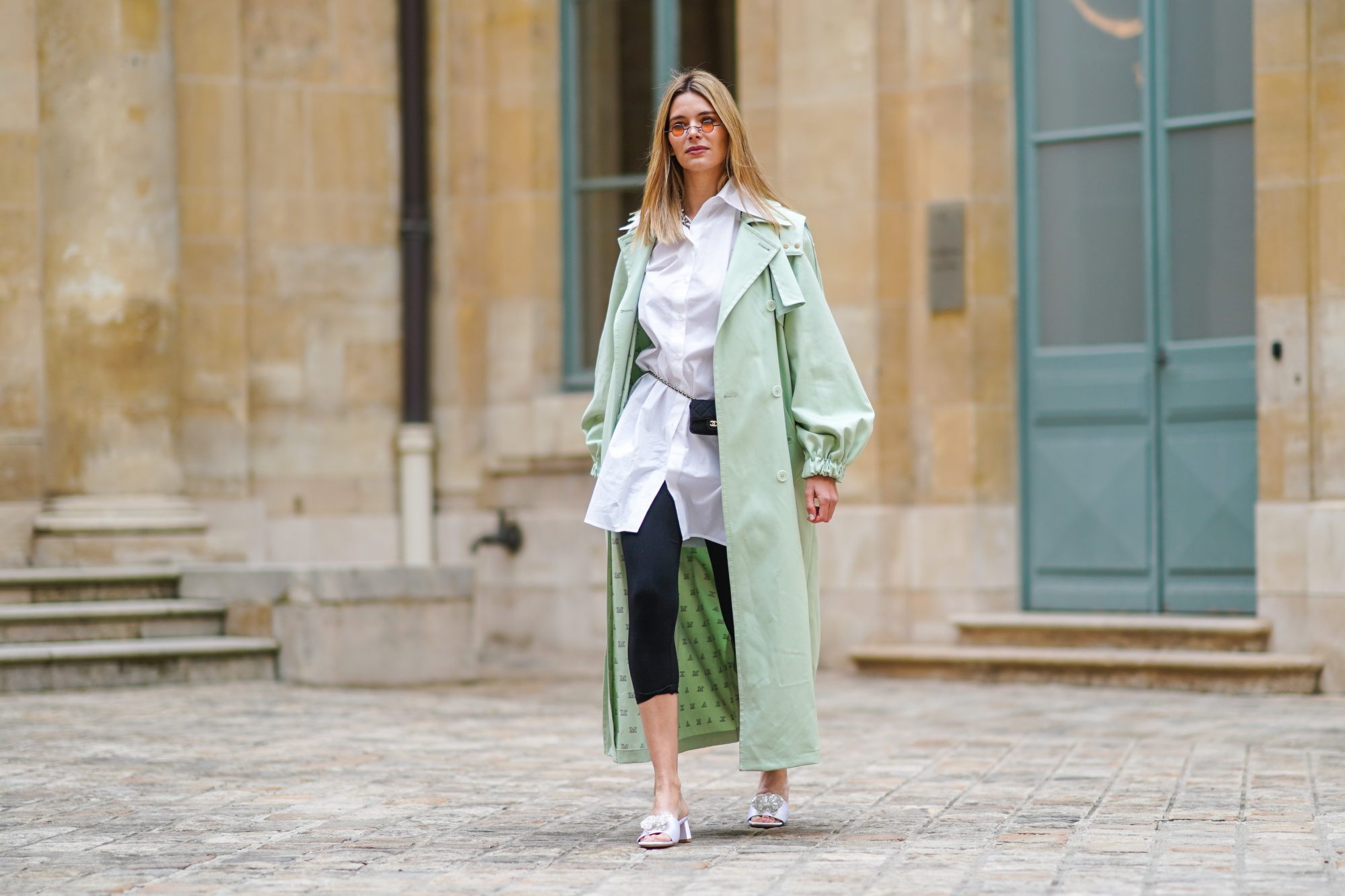 PARIS, FRANCE - MARCH 04: Natalia Verza @mascarada.paris wears sunglasses, a pale pastel mint green long trench coat from Max Mara, a white long shirt, a mini Chanel belt bag, black leggings, white sandals Bling Bling Alzuarr, on March 04, 2021 in Paris, France. (Photo by Edward Berthelot/Getty Images)