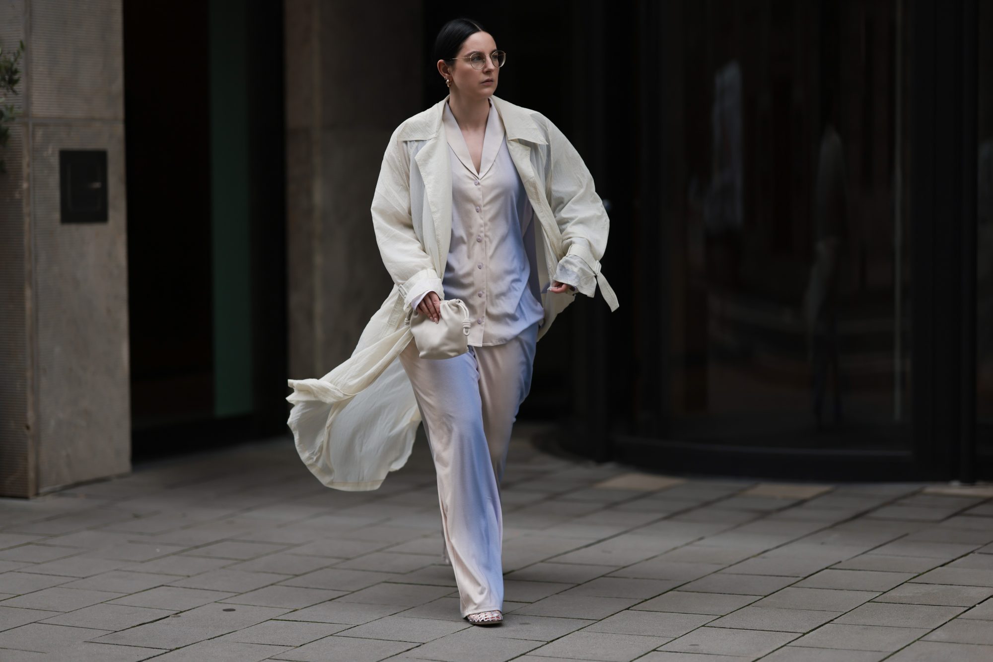 COLOGNE, GERMANY - AUGUST 23: Maria Barteczko seen wearing Ray-Ban gold round retro glasses, Hanro colorful ombré pyjama cotton set, The Frankie Shop cream white transparent lightweight trench coat, LOEWE cream white Flamenco small bag and The Row transparent jelly Mara flat shoes, on August 23, 2024 in Cologne, Germany. (Photo by Jeremy Moeller/Getty Images)