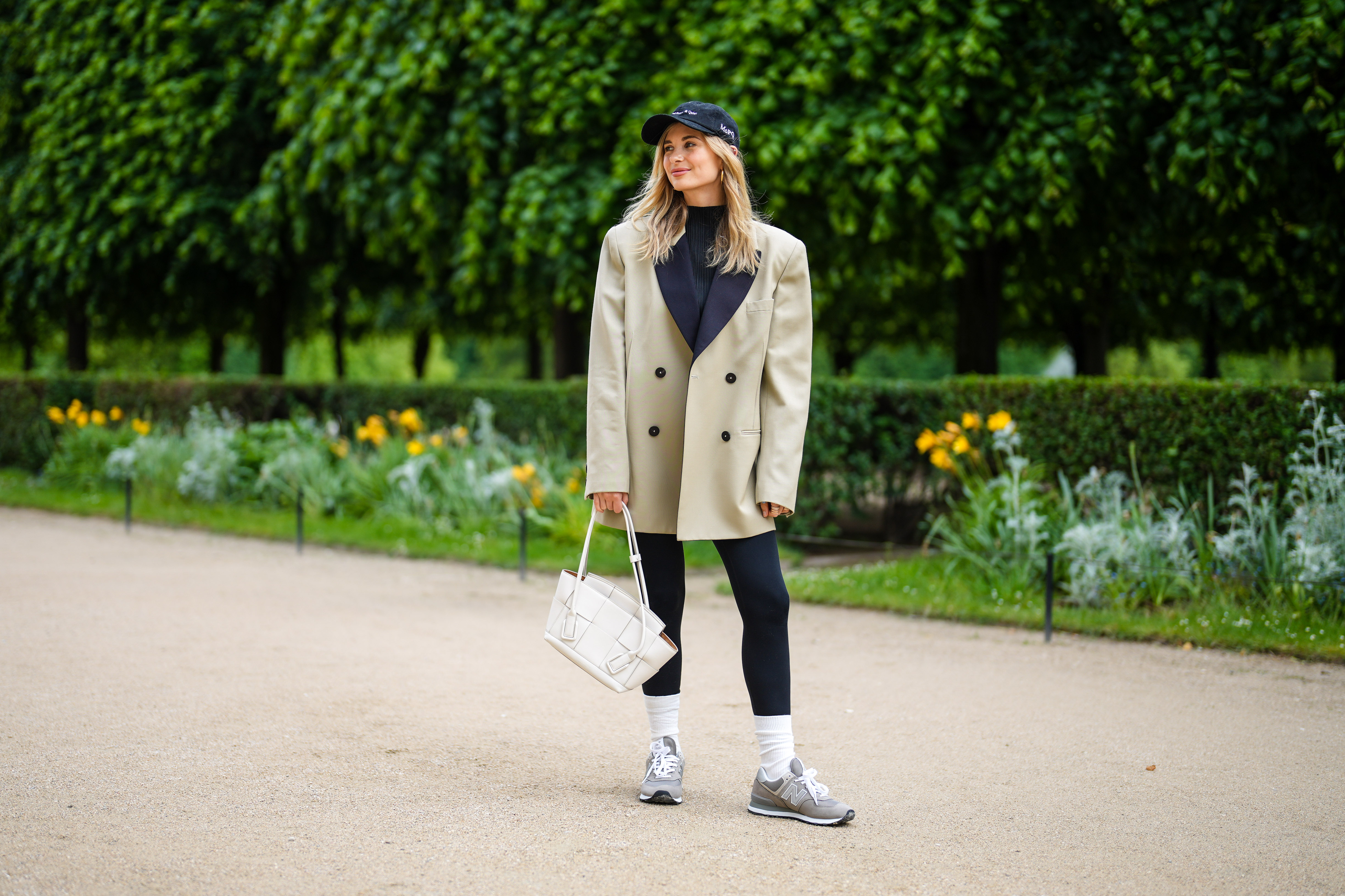 PARIS, FRANCE - MAY 27: Xenia Adonts wears a black cap from Museum of Peace and Quiet, a black ribbed turtleneck pullover, a beige long oversized jacket from Attire The Studio, black leggings from Nike, a white matte leather Bottega Veneta handbag, white socks, gray sneakers from New Balance, gold pink rings, on May 27, 2021 in Paris, France. (Photo by Edward Berthelot/Getty Images)