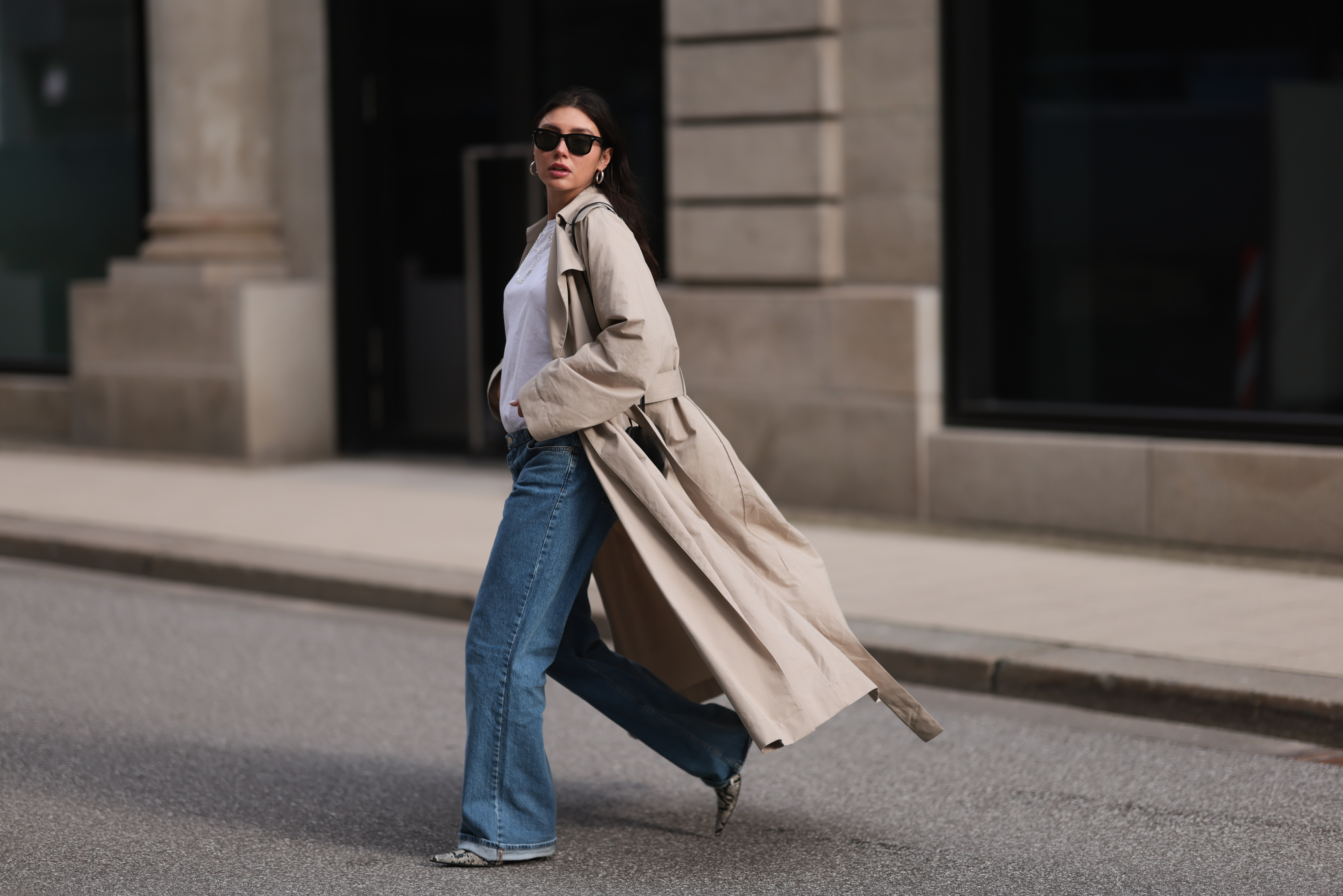 HAMBURG, GERMANY - FEBRUARY 23: Milena Karl seen wearing Ray-Ban black Wayfarer sunglasses, silver earrings, Hermès silver chain / necklace, The Row beige oversized long coat, NA-KD blue denim wide leg jeans / pants, COS white cotton basic shirt, Alaia black leather heart shaped crossbody bag and Ganni beige snake pattern leather heeled boots, on February 23, 2024 in Hamburg, Germany. (Photo by Jeremy Moeller/Getty Images)