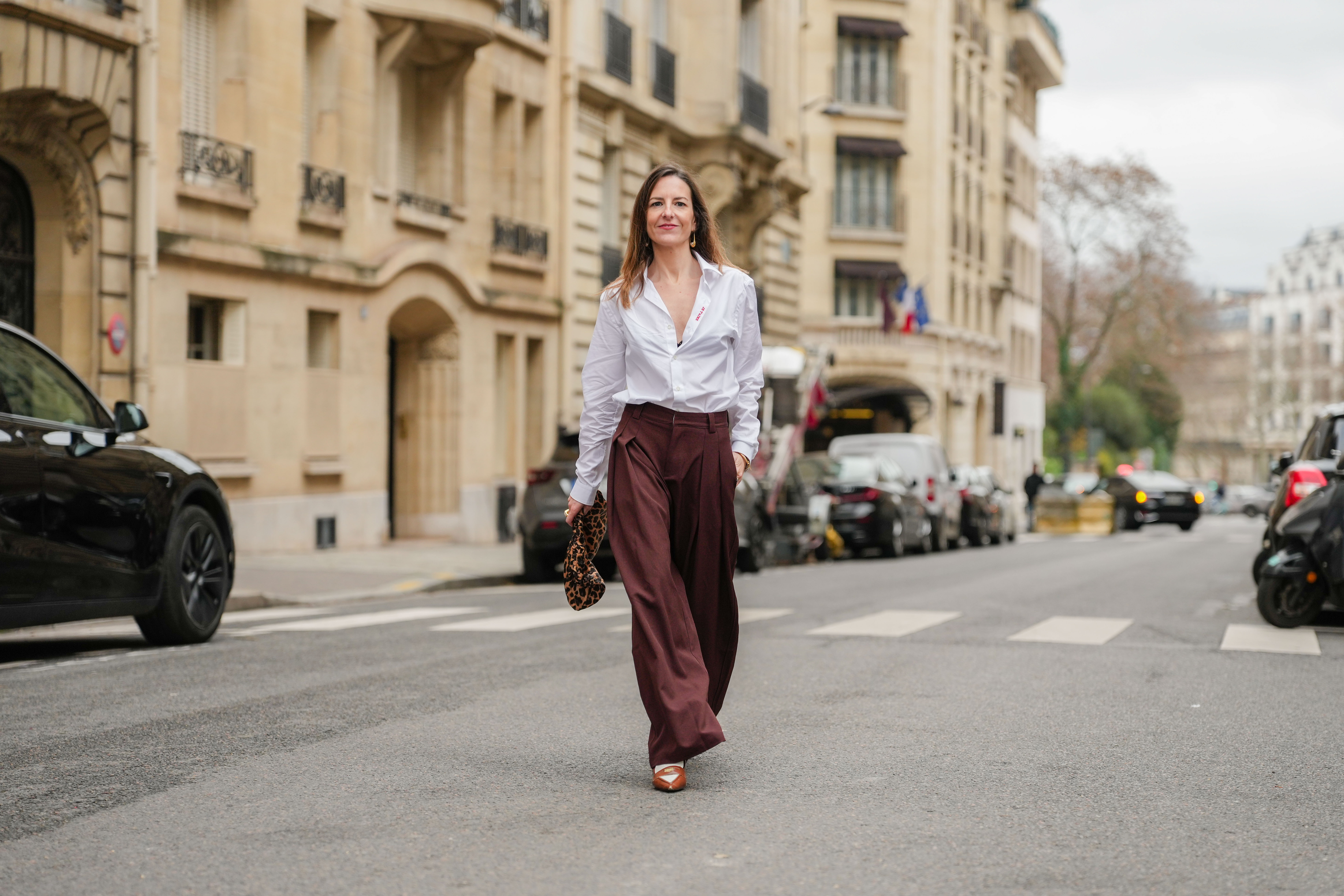 PARIS, FRANCE - DECEMBER 18: Alba Garavito Torre wears a white Figaret shirt, dark brown wide-leg Prassos pants, a brown Tras mi Bolsa bag with leopard patterns, tobacco heels slingback penny loafers from Miu Miu, during a street style fashion photo session, on December 18, 2024 in Paris, France. (Photo by Edward Berthelot/Getty Images)