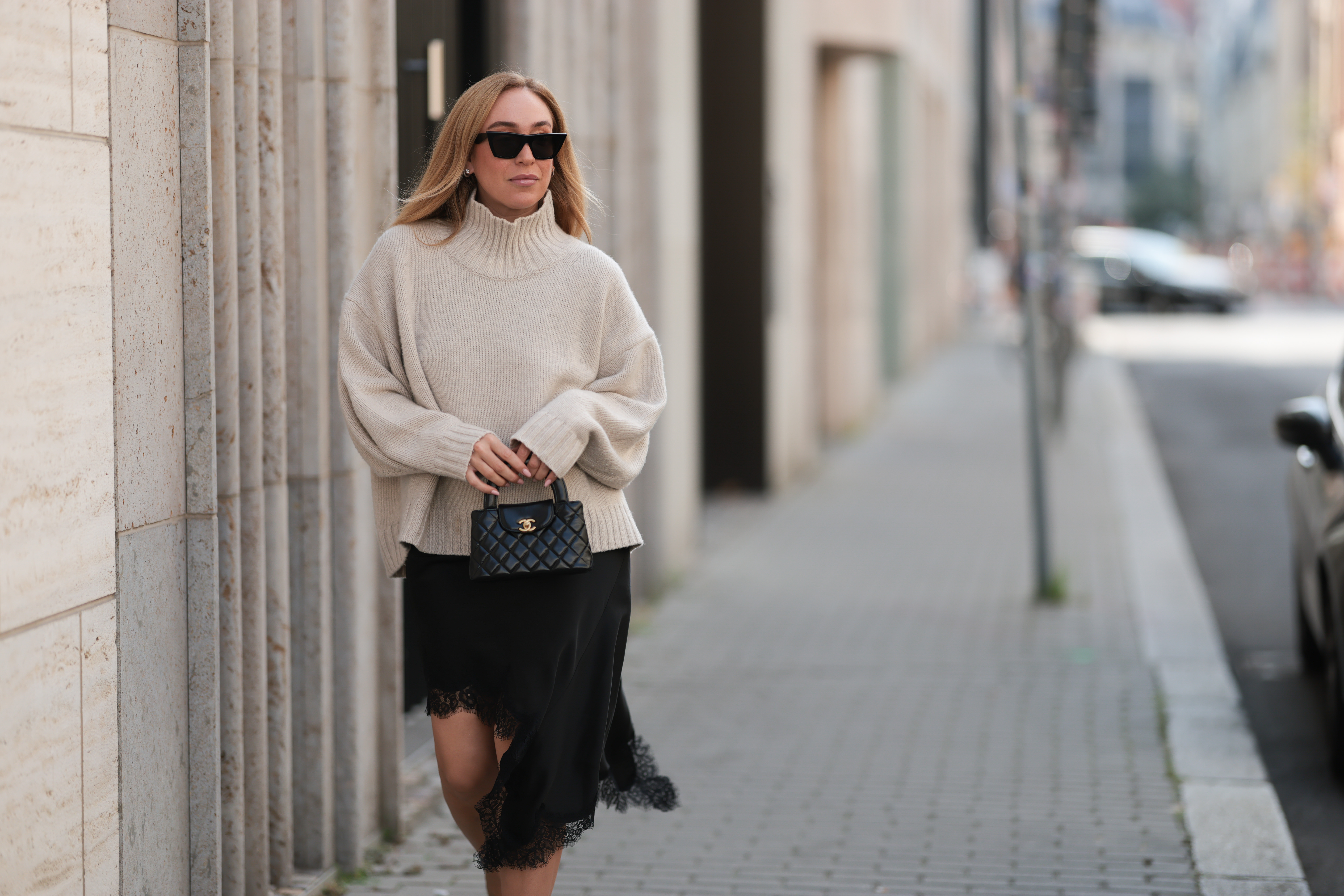 BERLIN, GERMANY - AUGUST 20: Sonia Lyson seen wearing Celine black cat-eye sunglasses, COS relaxed oversized beige turtleneck sweater in a chunky knit with dropped shoulders, Zara black asymmetrical slip dress featuring delicate lace trim along the hem and Chanel small black quilted top-handle Kelly bag with gold CC logo hardware, on August 20, 2025 in Berlin, Germany. (Photo by Jeremy Moeller/Getty Images)