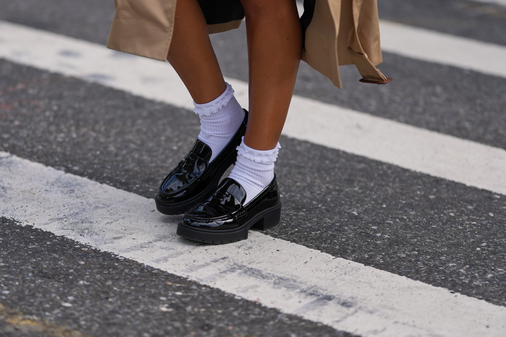 NEW YORK, NEW YORK - SEPTEMBER 15: A guest wears a beige trench coat, black patent varnished leather chunky lug-sole loafers shoes worn with white crew socks, outside Coach, during New York Fashion Week, on September 15, 2025 in New York, New York (Photo by Edward Berthelot/Getty Images)