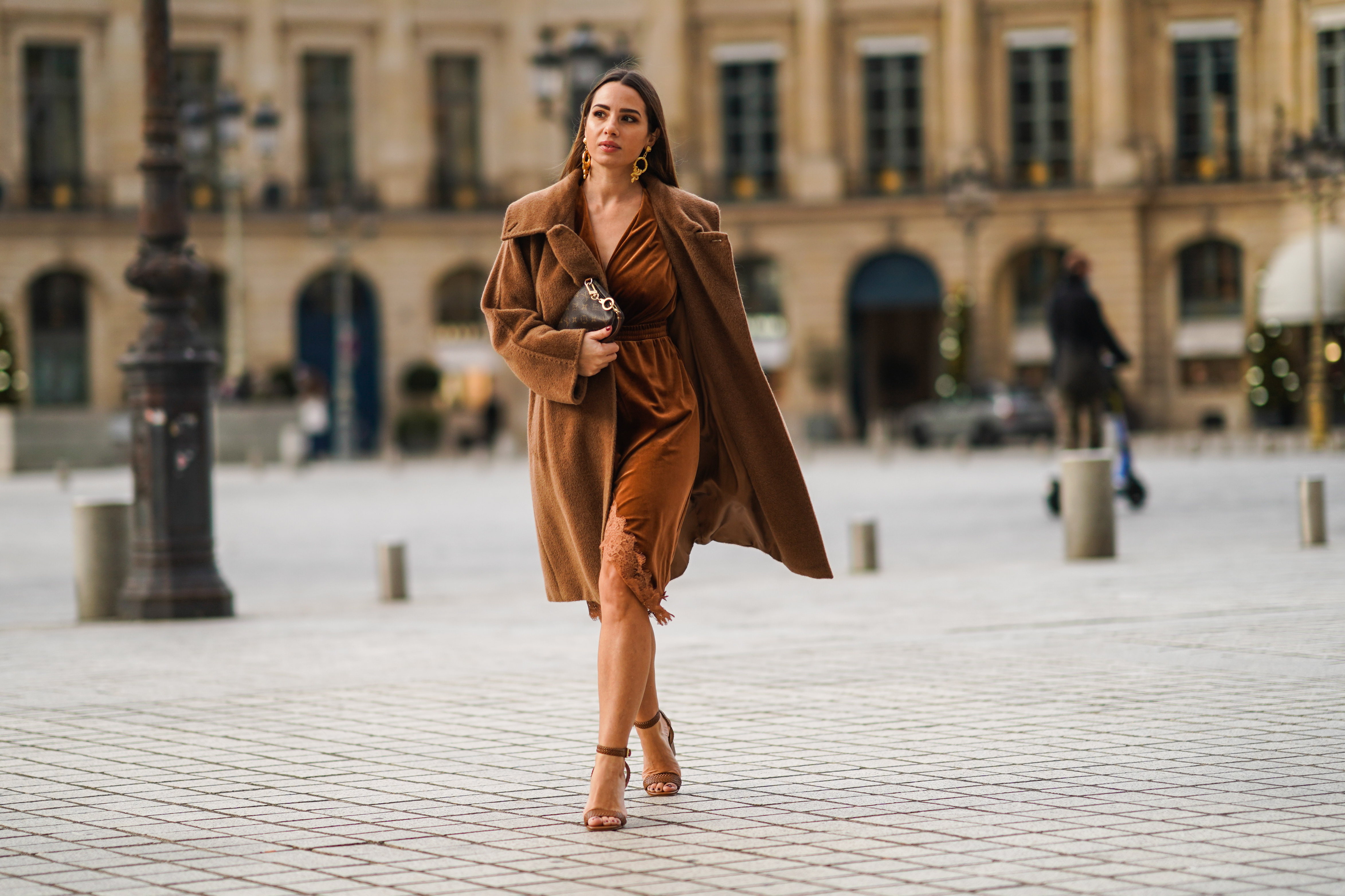 Maria Rosaria Rizzo wears golden long earrings from Raspini, a brown fluffy long winter coat from Max Mara, a brown leather monogram Vuitton bag, a brown velvet low-neck v-neck dress with lace and floral embroidery on the bottom part from Imprevu, brown high heeled shoes from Michael Kors, on December 04, 2020 in Paris, France.