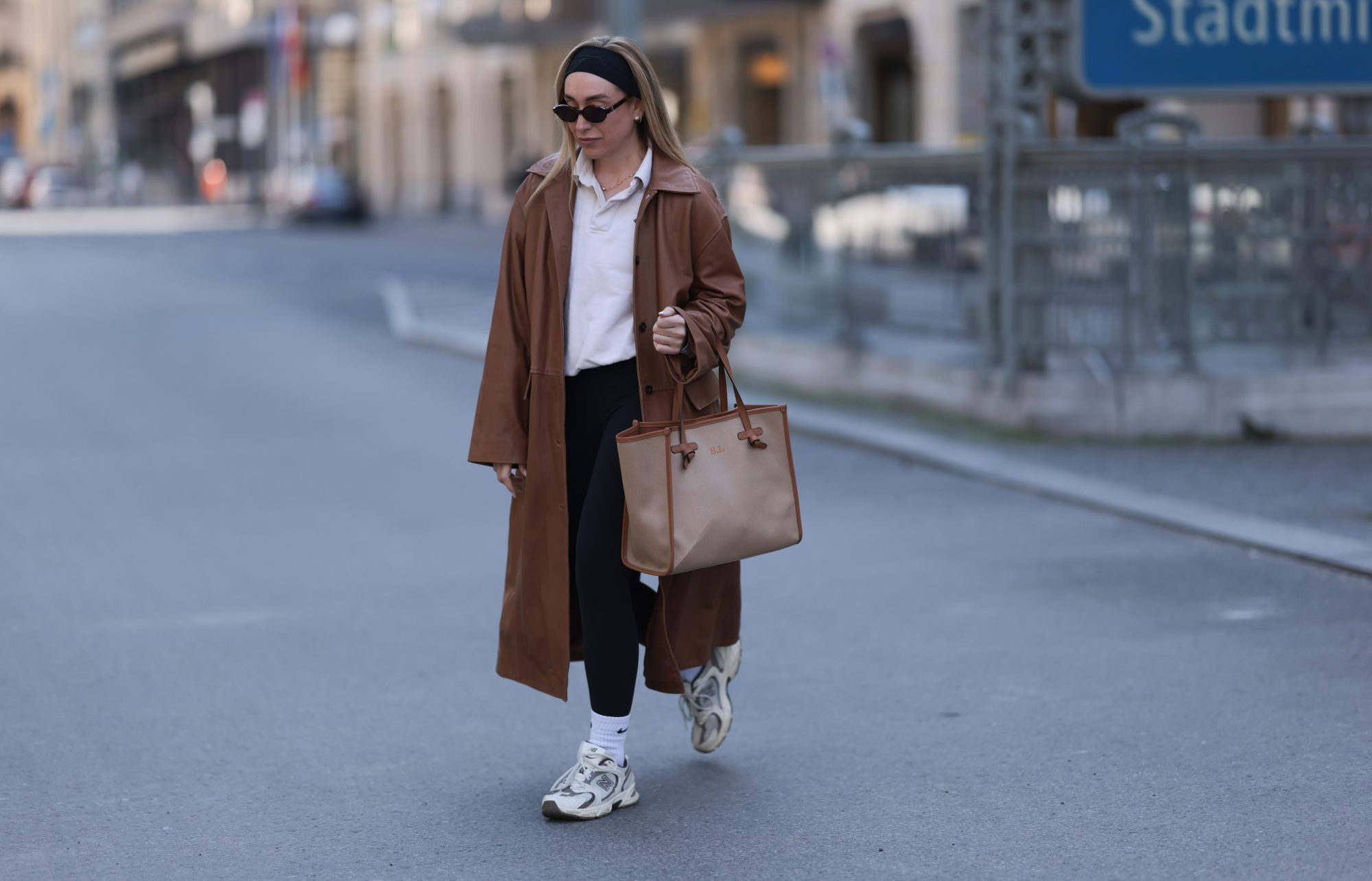 BERLIN, GERMANY - APRIL 09: Sonia Lyson seen wearing black cotton headband, Corlin Eyewear slim oval-shaped dark brown sunglasses, Worst Behavior white cotton polo sweater giving the look a sporty, laid-back vibe, Herskind long, cognac brown leather trench coat, Lululemon simple black comfortable and athleisure-inspired leggings, Gianni Chiarini large beige tote bag with brown leather trim and monogrammed initials, Nike white cotton crew socks and New Balance chunky cream white sneakers, on April 09, 2025 in Berlin, Germany. (Photo by Jeremy Moeller/Getty Images)