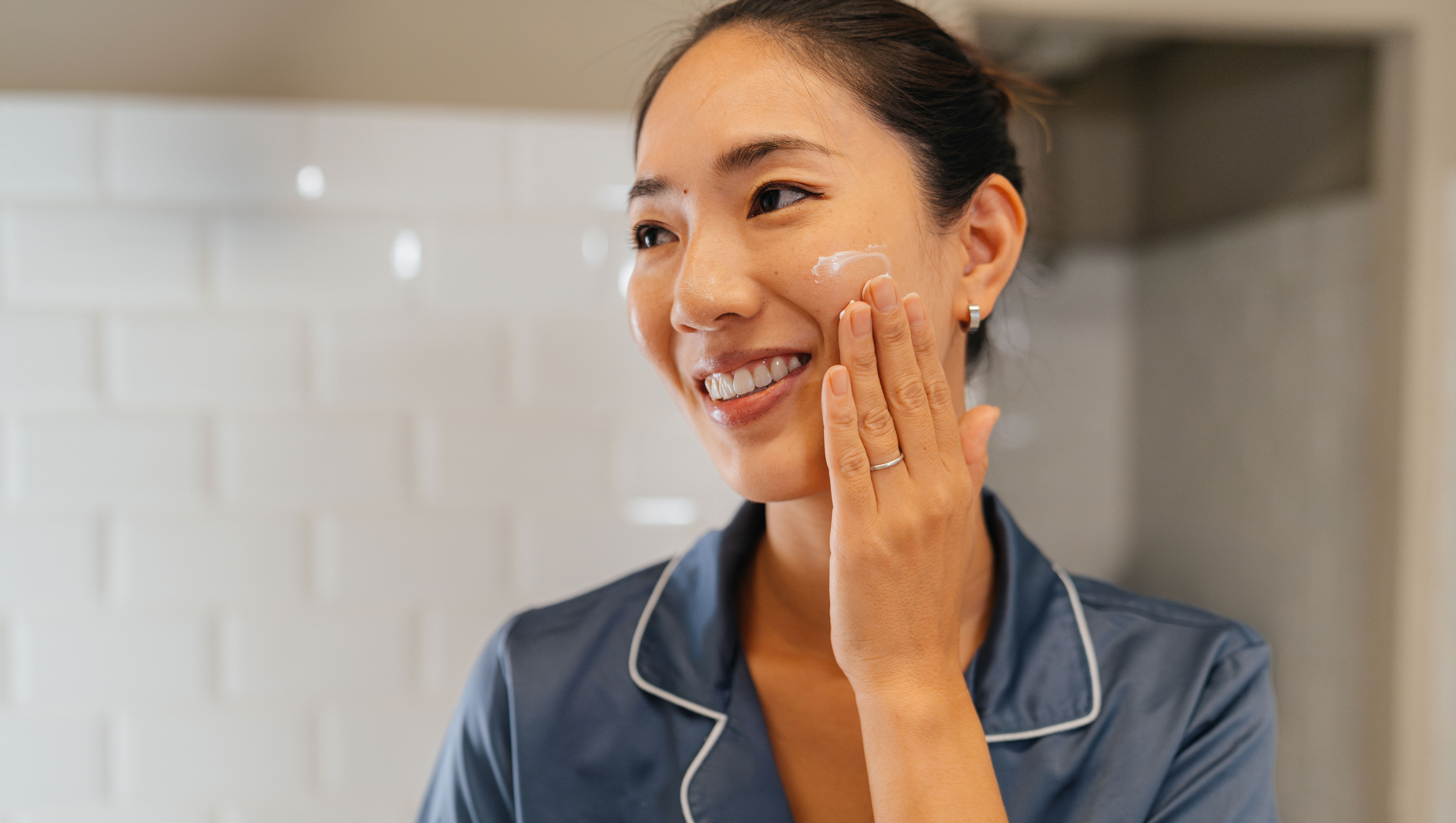Japanese woman looking her skin in the mirror, applying facial creme and preparing her self before going to work in the bathroom