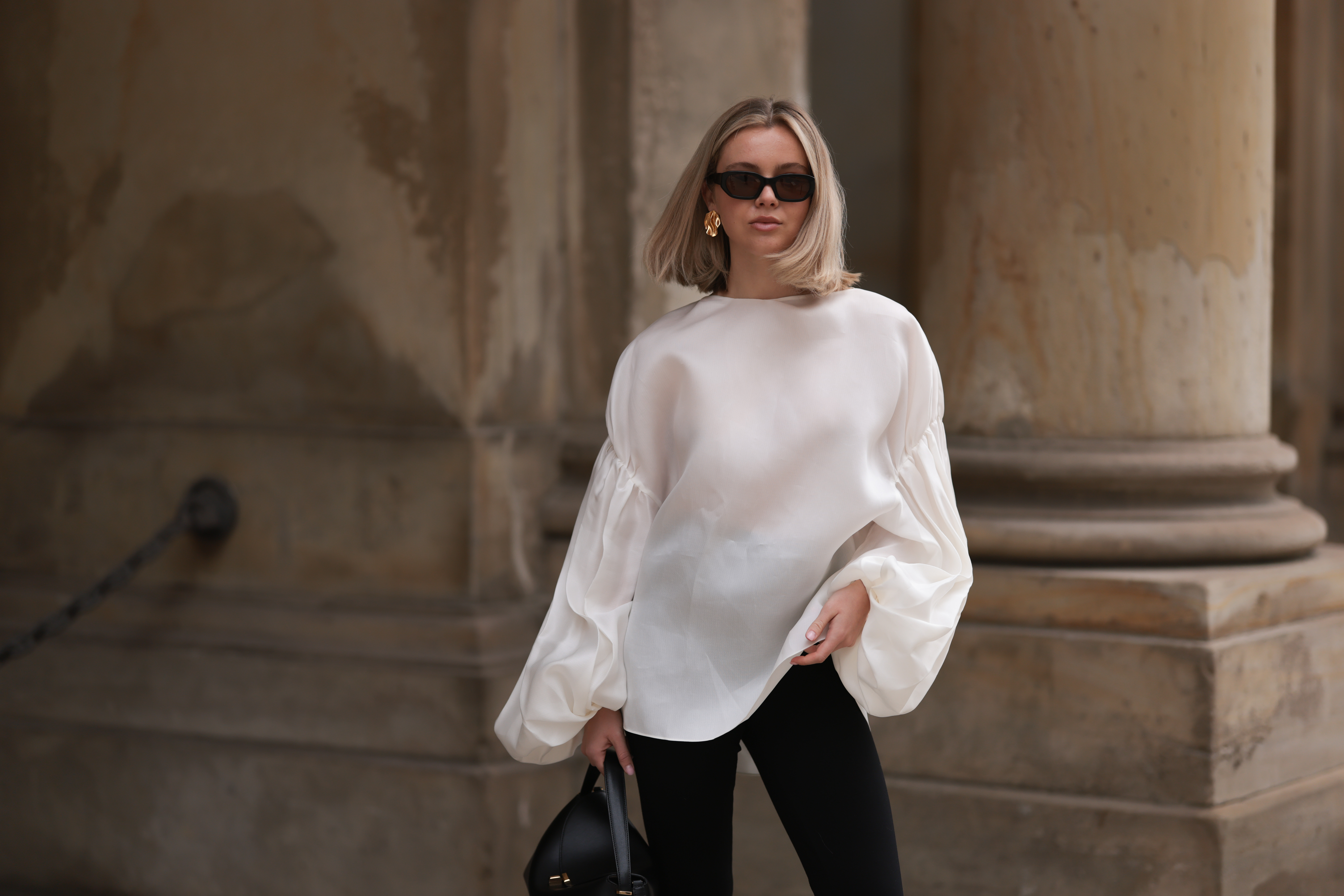 HAMBURG, GERMANY - APRIL 05: Isabelle Hartmann seen wearing Vehla Eyewear black / brown sunglasses, Nootka gold earrings, Khaite oversized puffy ruffled long sleeve silk top, Isabelle Hartmann x Edited black slit pants and Toteme black leather bag on April 05, 2024 in Hamburg, Germany. (Photo by Jeremy Moeller/Getty Images)