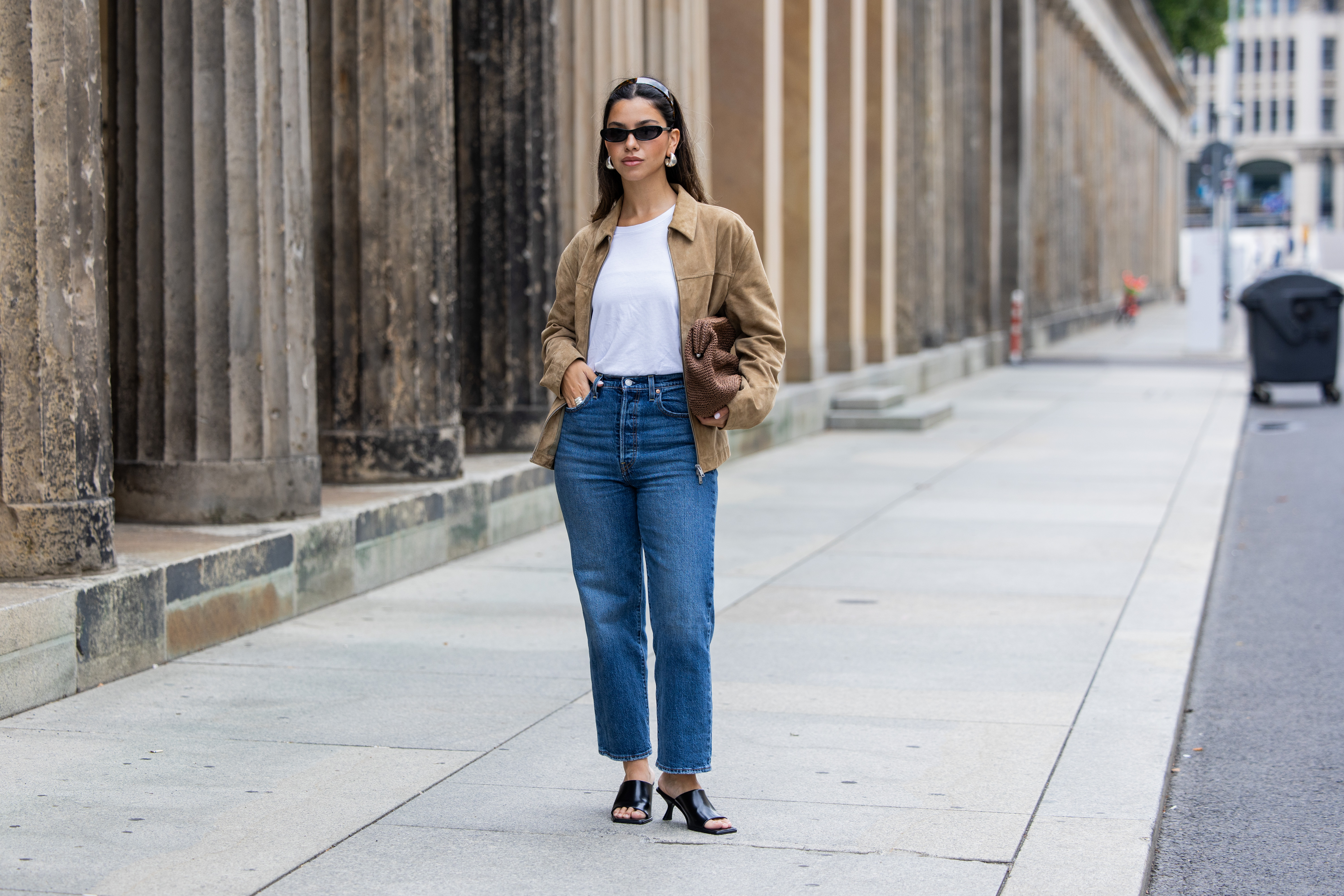 Bella Emar wears Levi’s blue denim jeans, white Cos t-shirt, brown Massimo Dutti Jacket, black H&M Heels, Mango sunglasses during the Berlin Fashion Week SS25 on July 01, 2024 in Berlin, Germany.