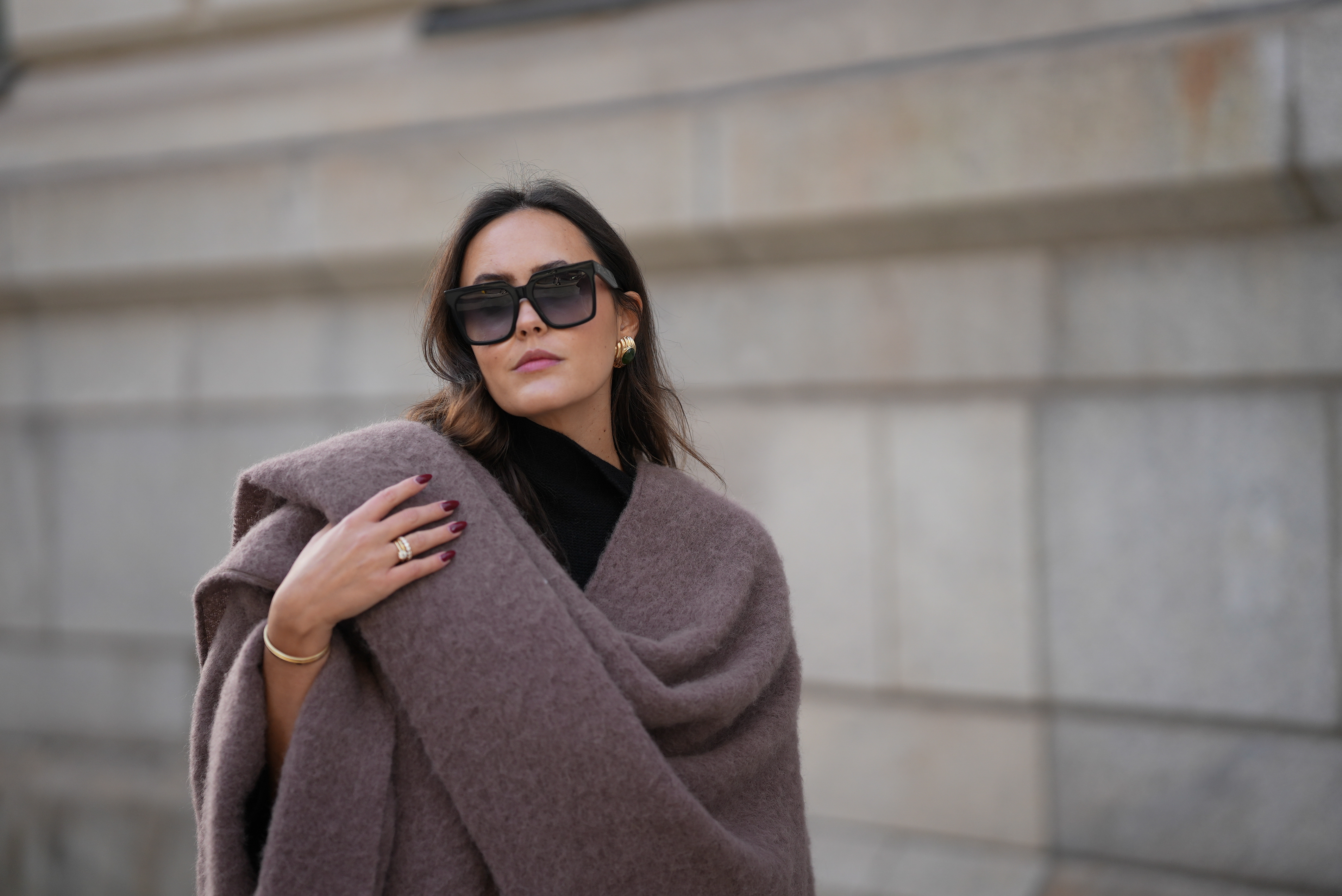 Laura Noltemeyer is seen wearing an oversized fringed wool poncho in a mauve tone with a textured, fluffy finish, fringes at the hem and a gold pin closure element called &bdquo;Poncho COZY&ldquo; by Aylin Koenig; black fine-knit turtleneck sweater with slim-fitting silhouette by Aylin Koenig; among her jewelry is a white gold &bdquo;LOVE&ldquo; bracelet by Cartier; oversized square black acetate sunglasses with ombr&eacute; tinted lenses by C&eacute;line; large gold statement earrings with a ruffled surface and a green stone element by Mango; her dark brown hair is styled in loose waves with a center part on November 13, 2025 in Hamburg, Germany.