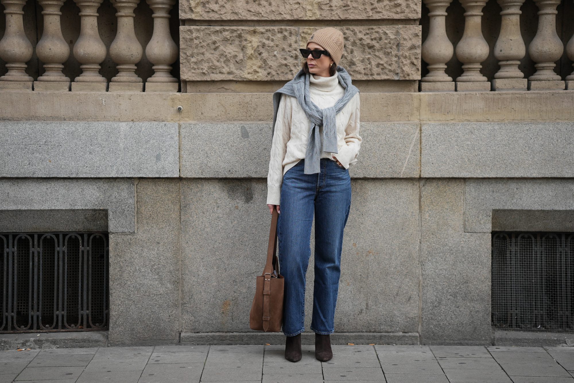 DUESSELDORF, GERMANY - NOVEMBER 10: Patricia Wirschke is seen wearing a cream cable-knit turtleneck sweater by Tommy Hilfiger; a light grey cable-knit sweater draped over her shoulders by Tommy Hilfiger; straight-leg blue jeans by Levi&rsquo;s; brown suede boots with a pointed toe by Massimo Dutti; a brown suede tote bag with a shoulder strap by Max Mara; black cat-eye sunglasses by Phoebe Philo; a beige ribbed beanie with an embroidered crest logo by Tommy Hilfiger; her brown hair is worn straight and tucked into the collar; gold &ldquo;Serpenti&rdquo; earrings by Bulgari on November 10, 2025 in Duesseldorf, Germany. (Photo by Moritz Scholz/Getty Images)