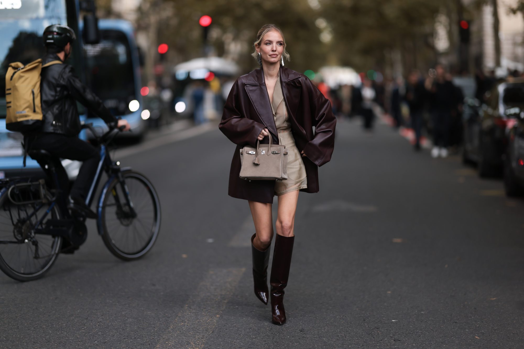 PARIS, FRANCE - SEPTEMBER 28: Leonie Hanne is seen wearing shiny silver earrings in a large organic shape from Alaïa; a burgundy leather coat with lapel collar from Hermès; a beige transparent set underneath, consisting of a shirt tucked into shorts; a gold ring; a beige suede “Birkin Grizzly“ bag from Hermès; and pointed shiny burgundy leather knee-high stiletto boots with a cylindrical shaft from Paris Texas before the Hermès Womenswear Spring/Summer 2025 Show as part of Paris Fashion Week on September 28, 2024 in Paris, France. (Photo by Jeremy Moeller/Getty Images)