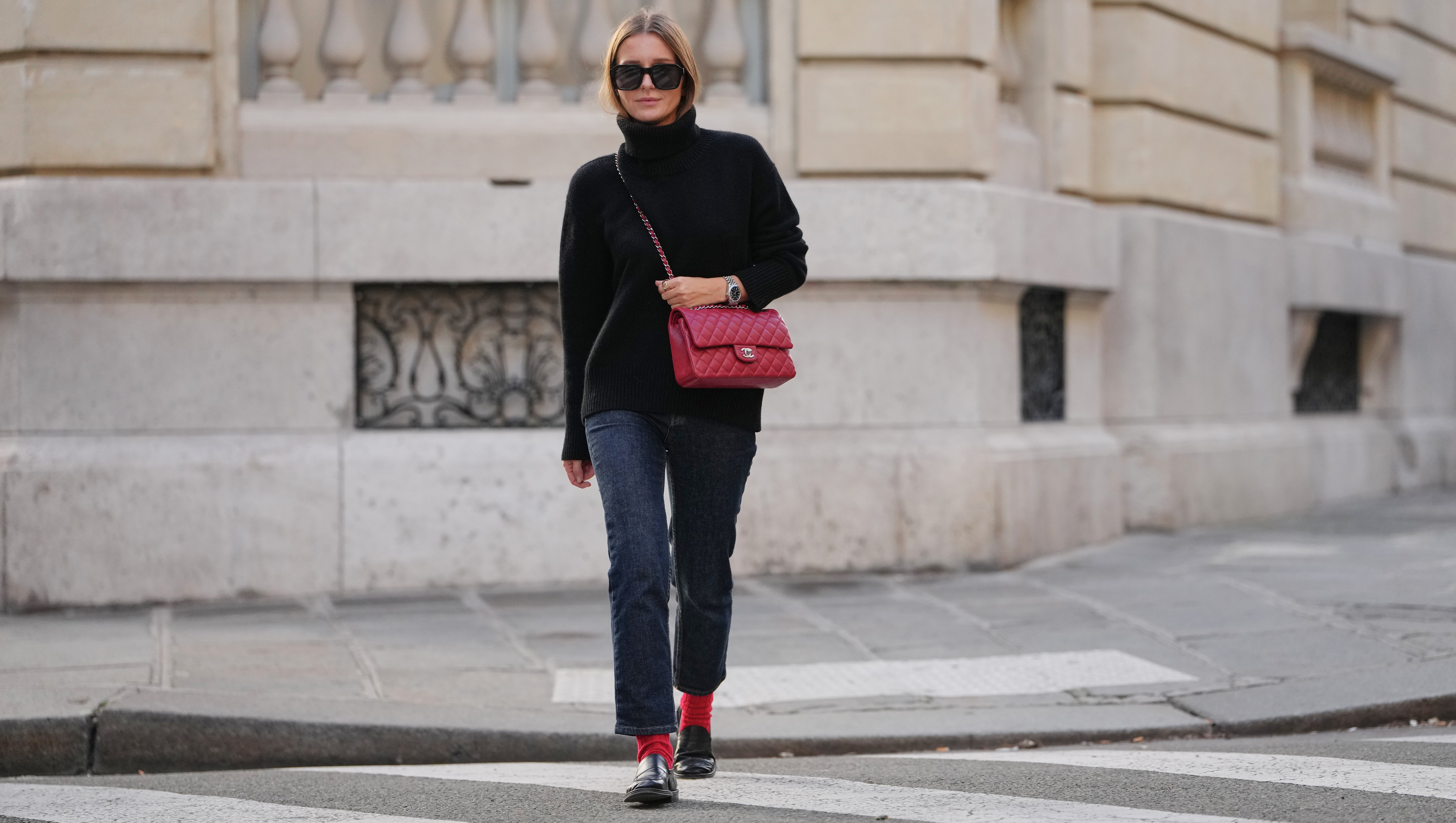 PARIS, FRANCE - DECEMBER 17: Diane Batoukina wears long straight brown hair with a center part, natural makeup with pastel pink lipstick, black sunglasses, a black wool turtleneck sweater, dark blue straight-leg jeans, red ribbed socks, black leather loafers shoes, a red quilted leather Chanel flap bag with chain strap, during a street style fashion photo session, on December 17, 2025 in Paris, France. (Photo by Edward Berthelot/Getty Images)