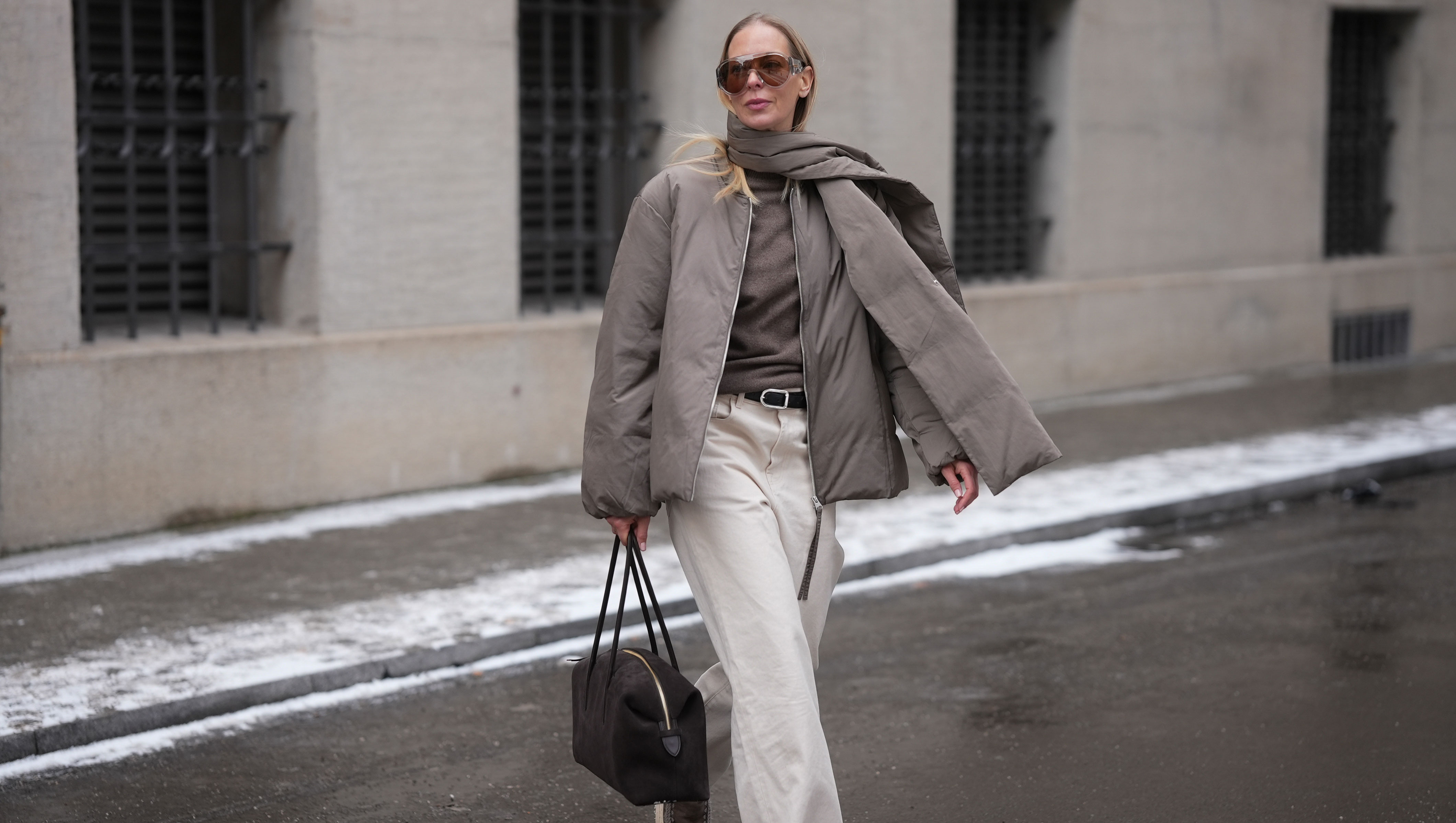 MUNICH, GERMANY - JANUARY 8: Mirja Klein is seen wearing a khaki padded jacket with an integrated scarf detail, a relaxed oversized silhouette and dropped shoulders from Arket; a brown cashmere knit sweater with a fine texture and classic crew neckline from Jacquemus; off white straight leg jeans with a high rise and structured cotton fabric from R&oacute;he Frames; a black leather belt with a metal buckle from Dehanche; a brown suede leather shoulder bag with a minimalist rectangular shape, top zipper and slim shoulder straps from Demellier London; oversized aviator style sunglasses with brown tinted lenses and a clear acetate frame from Bottega Veneta; her long blond straight hair is worn loose on January 8, 2026 in Munich, Germany. (Photo by Moritz Scholz/Getty Images)