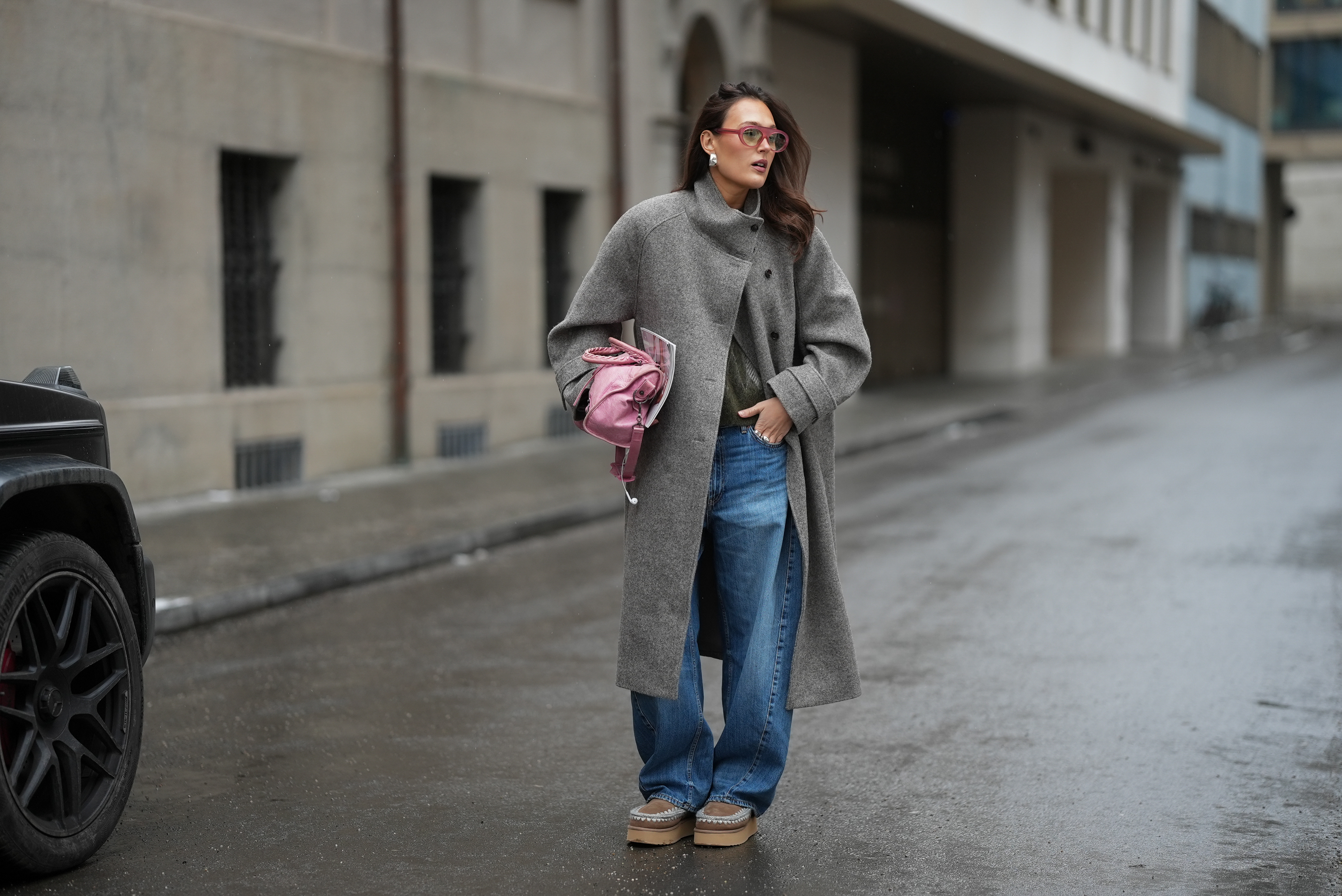 Amanda M&uuml;hle is seen wearing a grey wool coat with wide lapels, button closure and buttoned collar from Siyazu; a patterned knit sweater in muted green and pink tone with a argyle pattern and soft wool blend texture from Marc O&rsquo;Polo Denim; a white cotton base layer T-shirt from COS worn underneath; blue denim jeans with a loose straight leg cut from Zara; beige suede Mou boots with a platform sole and signature stitched detailing from Mou; a pink leather Balenciaga &ldquo;City bag&rdquo; with a softly slouched shape, top handles and silver hardware from Balenciaga; multiple silver rings from Pilgrim; holding a Vogue Magazine; aviator style glasses with a pink tinted frame and slightly tinted lenses from Lexxola; silver statement earrings with a sculptural finish from Mango; her long brown hair is worn loose and side parted on January 8, 2026 in Munich, Germany.