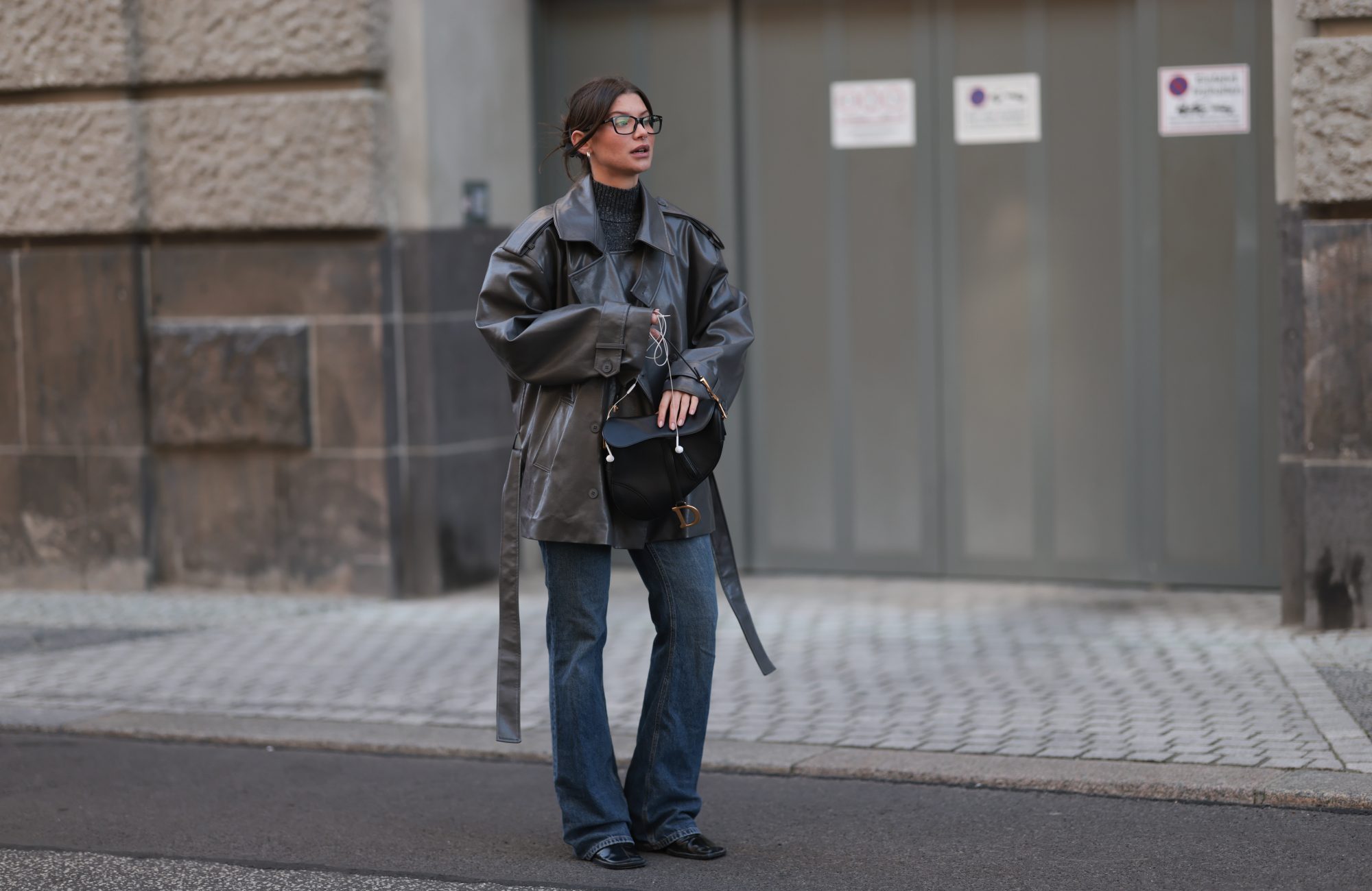 BERLIN, GERMANY - NOVEMBER 07: Sophia Geiss with brown hair seen wearing a long grey black leather coat from Source Unknown layered over a grey Zara pullover, styled with light blue Mango jeans and black Jil Sander boots. She accessorizes her look with a black Christian Dior Saddle bag featuring gold hardware and classic black Ray-Ban sunglasses on November 07, 2025 in Berlin, Germany. (Photo by Jeremy Moeller/Getty Images)
