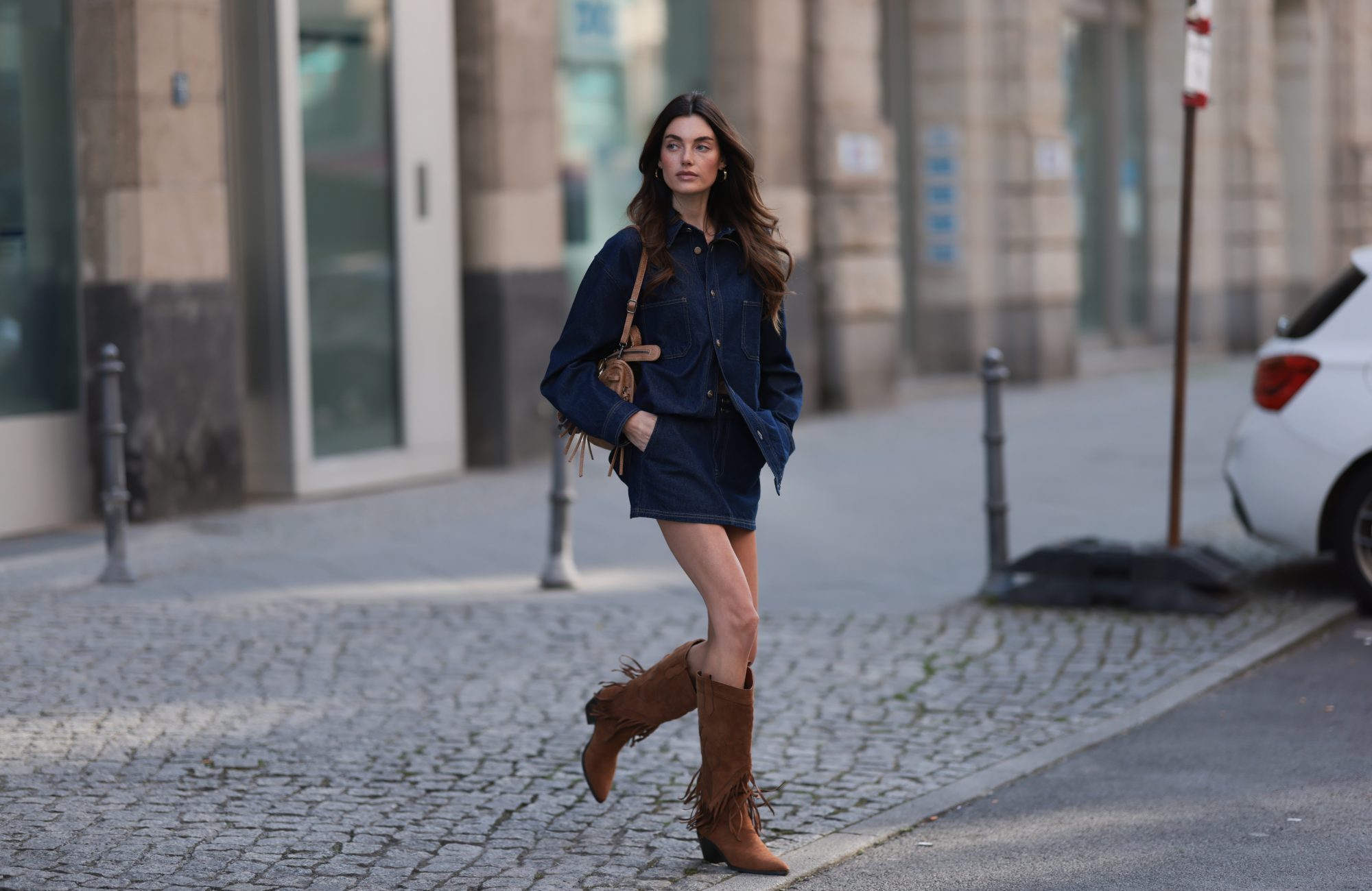 BERLIN, GERMANY - MARCH 21: Celine Bethmann seen wearing Cie Cie oversized dark-wash denim button-up western-inspired shirt with a relaxed fit, matching Cie Cie high-waisted dark blue denim mini skirt, vintage brown / tan suede leather handbag with braided handles and fringe elements and Steve Madden brown suede leather statement knee-high suede boots with fringe elements, on March 21, 2025 in Berlin, Germany. (Photo by Jeremy Moeller/Getty Images)