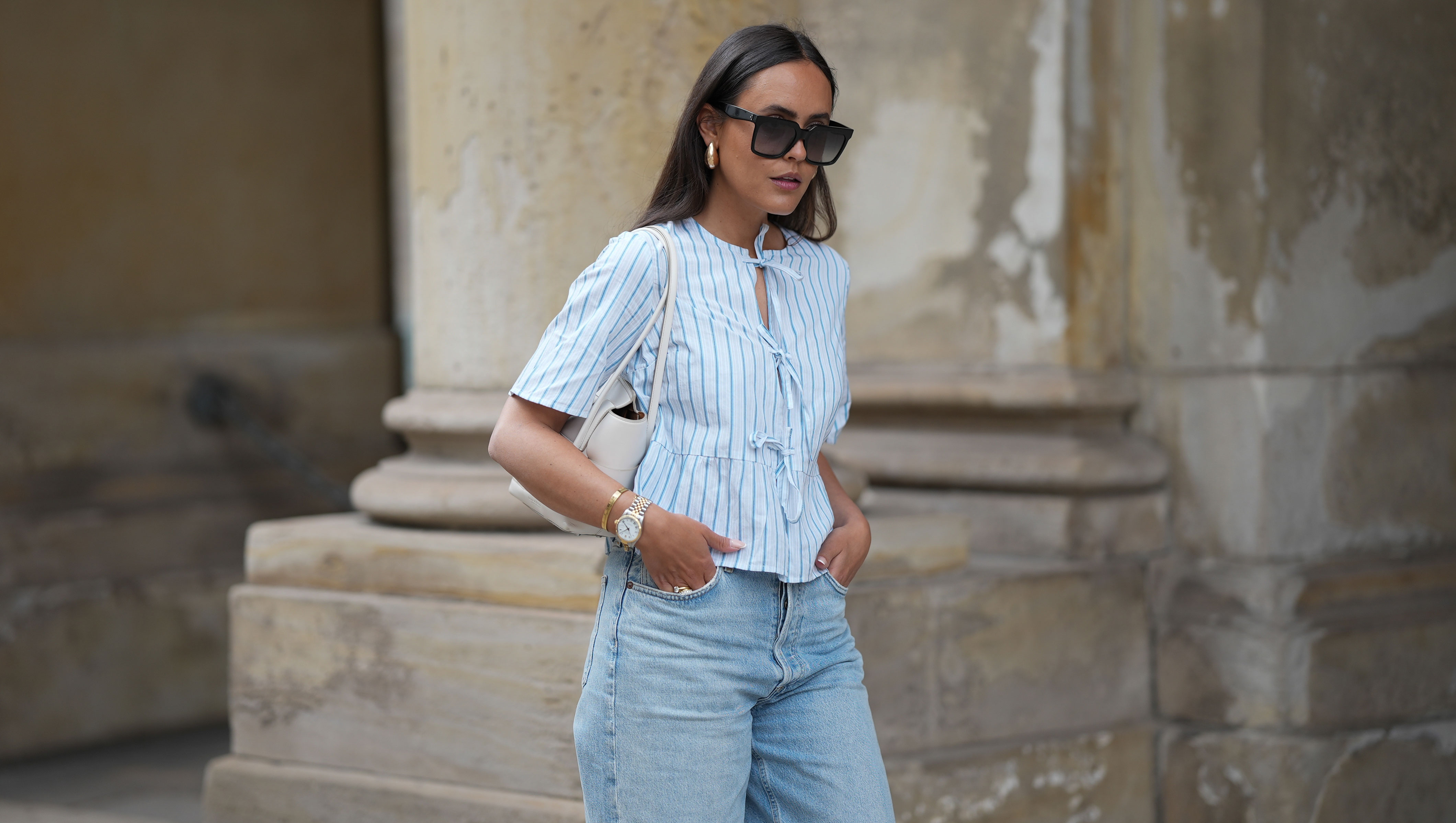 HAMBURG, GERMANY - MAY 7: Laura Noltemeyer is seen wearing a light indigo blue wide leg jeans from Agolde, a cotton puff sleeve blouse with ties in the front in white with blue stripes from Sézane, black oversized cat-eye acetate sunglasses from Celine, Arco handbag in white intrecciato leather from Bottega Veneta, big golden drop-shaped earrings, a small Lady-Datejust watch in gold-silver from Rolex, a golden LOVE bracelet from Cartier, stacked golden rings from Cartier on May 7, 2025 in Hamburg, Germany. (Photo by Moritz Scholz/Getty Images)