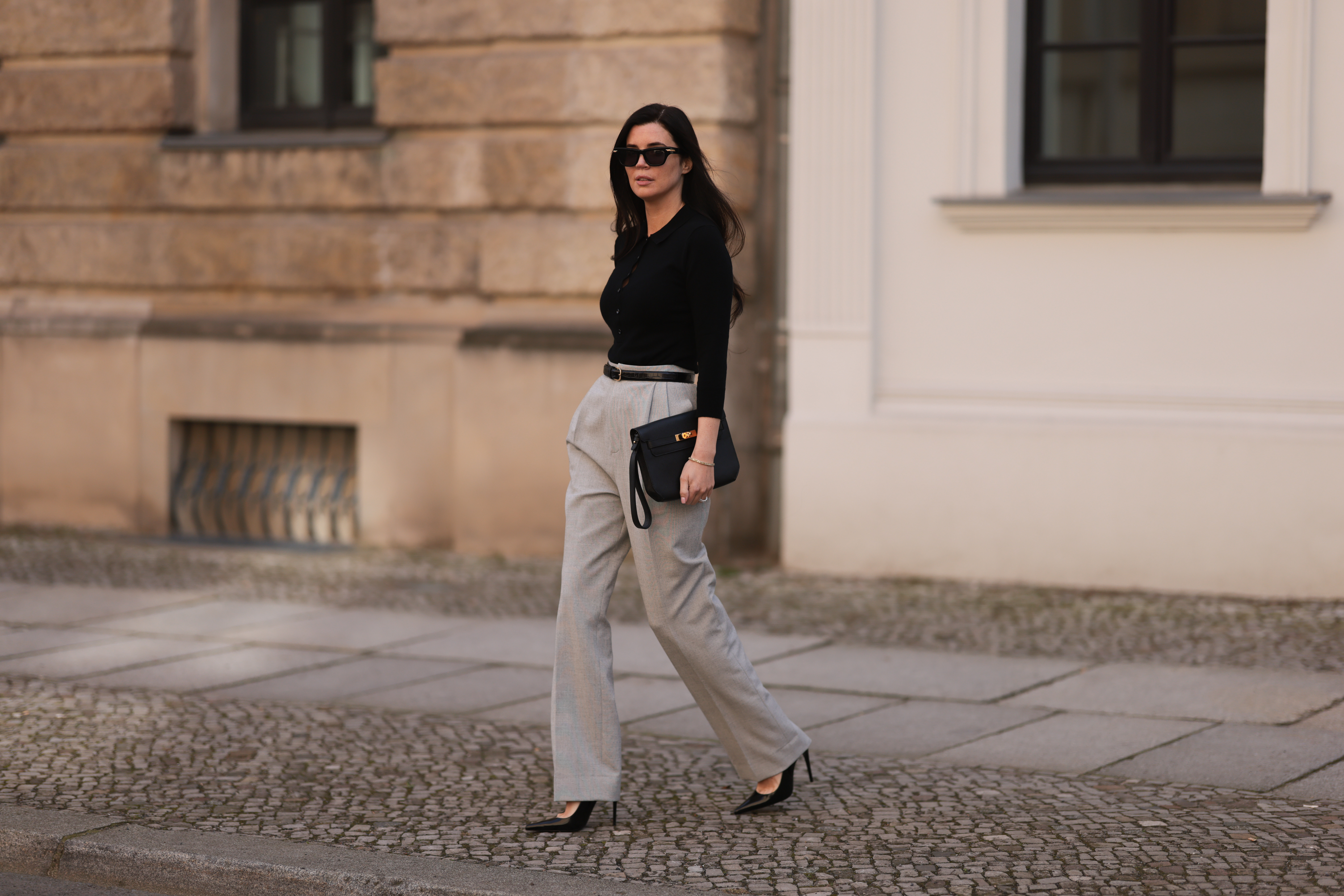 Leo Eberlin seen wearing Bottega Veneta black sunglasses, Leo Mathild jewelry / diamond bracelet and rings, Allude x Leo Mathild cashmere wool knit buttoned body, Toteme black leather belt, Velaa light grey elegant suit pants, Hermès black leather clutch bag and Saint Laurent black varnished leather heels / pumps, on February 25, 2024 in Berlin, Germany.