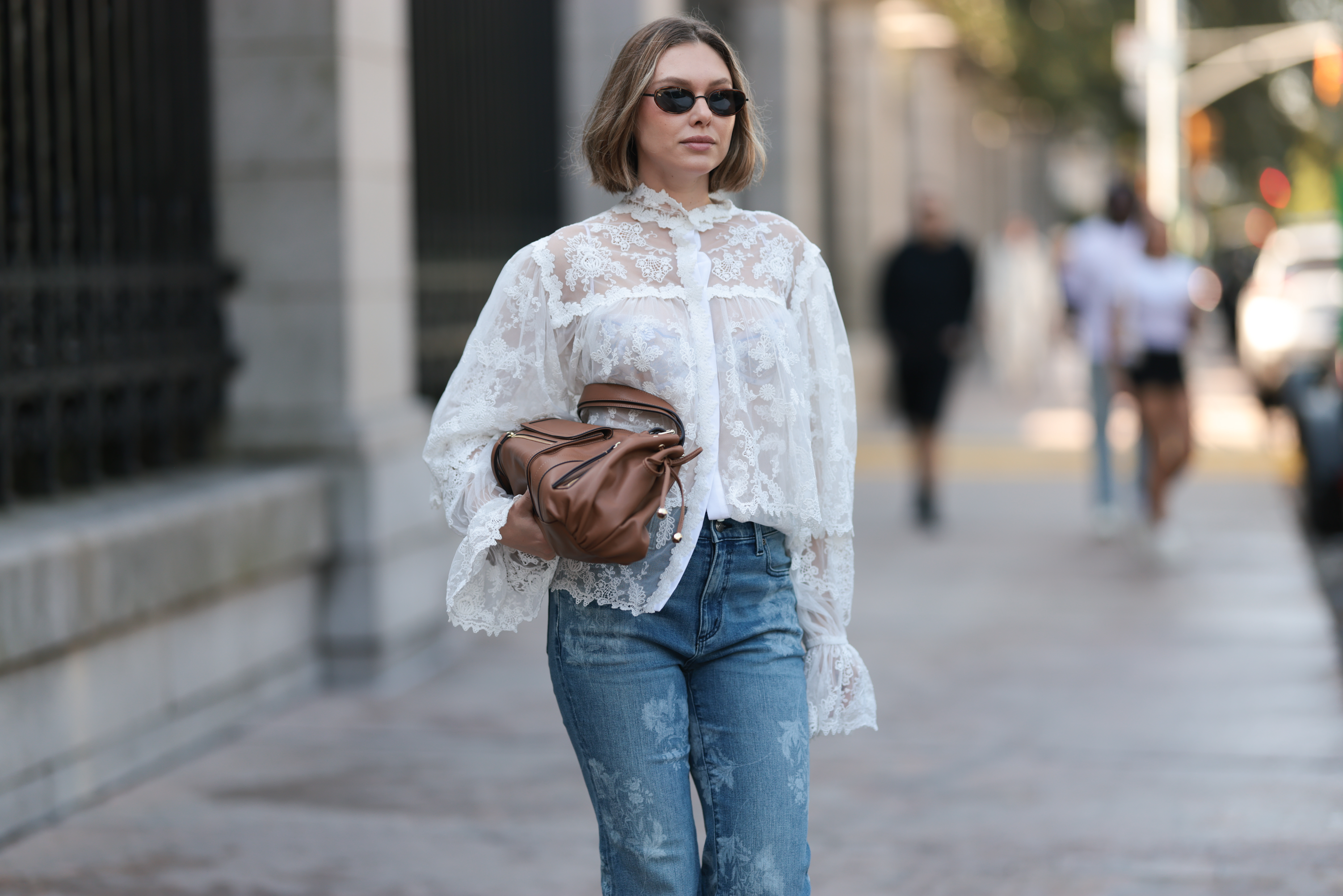 NEW YORK, NEW YORK - SEPTEMBER 14: Kate Smolianinova seen wearing Vehla Eyewear slim rectangular sunglasses in a dark brown. Her hair styled in a sleek chin-length bob with a soft middle part. A Kobi Halperin sheer white lace blouse with floral embroidery, high ruffled collar, voluminous sleeves and scalloped edges, paired with Kobi Halperin blue high-waist flared jeans featuring tonal floral jacquard detailing and a Gerard Darel soft brown leather handbag with gathered pleats and rounded handles, outside the Ulla Johnson show, during New York Fashion Week, on September 14, 2025 in New York City. (Photo by Jeremy Moeller/Getty Images)