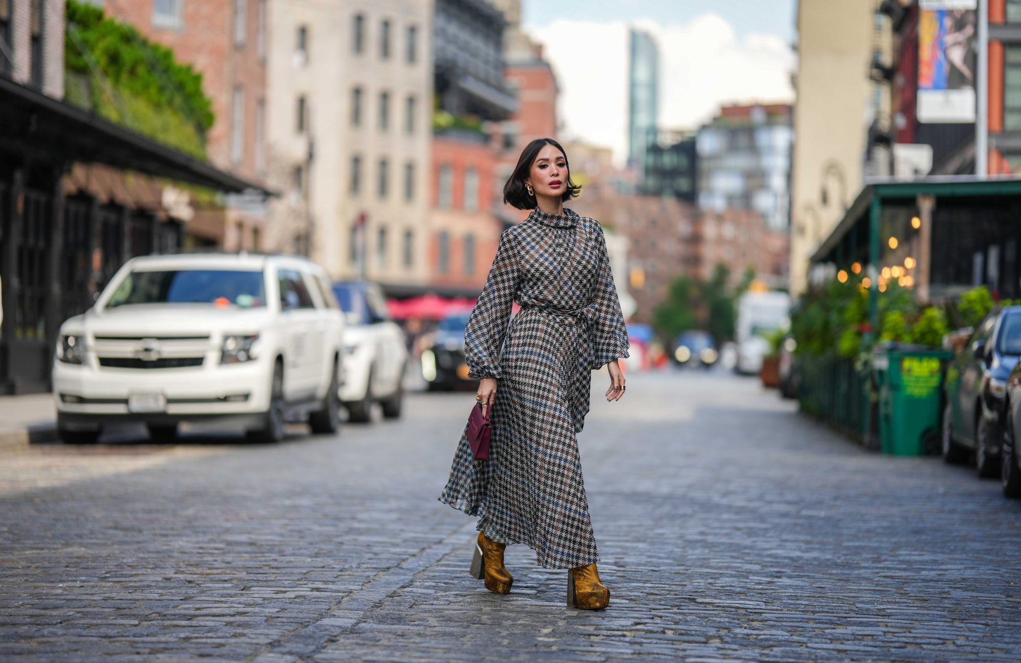 NEW YORK, NEW YORK - SEPTEMBER 12: Heart Evangelista wears golden earrings, a houndstooth pattern printed midi pleated dress, a burgundy leather bag from Carolina Herrera, golden floral print platform boots, outside Carolina Herrera, during New York Fashion Week, on September 12, 2023 in New York City. (Photo by Edward Berthelot/Getty Images)