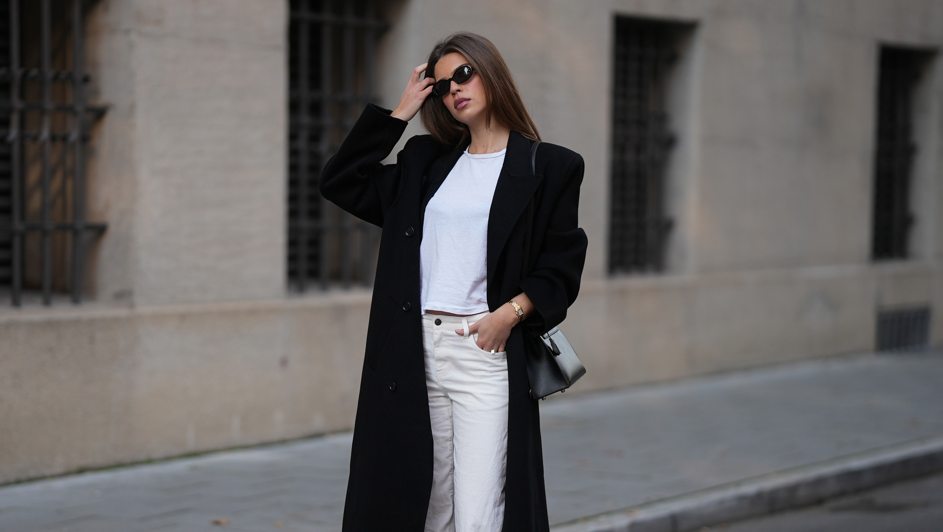 MUNICH, GERMANY - NOVEMBER 5: Iva Nikolina is seen wearing a long black wool coat with structured shoulders and a straight silhouette by Almada Label; a white fitted cotton crewneck T-shirt by Re/Done; white wide-leg jeans in a straight leg cut by The Row; black polished leather loafers with a gold logo detail by Saint Laurent; a structured black leather &sbquo;&Auml;&uacute;Kelly&sbquo;&Auml;&ugrave; handbag with silver hardware by Herm&radic;&reg;s; a small gold &sbquo;&Auml;&ucirc;Panth&radic;&copy;re&sbquo;&Auml;&uacute; watch by Cartier; narrow oval black sunglasses by Selima Optique; her brown hair is worn straight and parted in the middle on November 5, 2025 in Munich, Germany. (Photo by Moritz Scholz/Getty Images)
