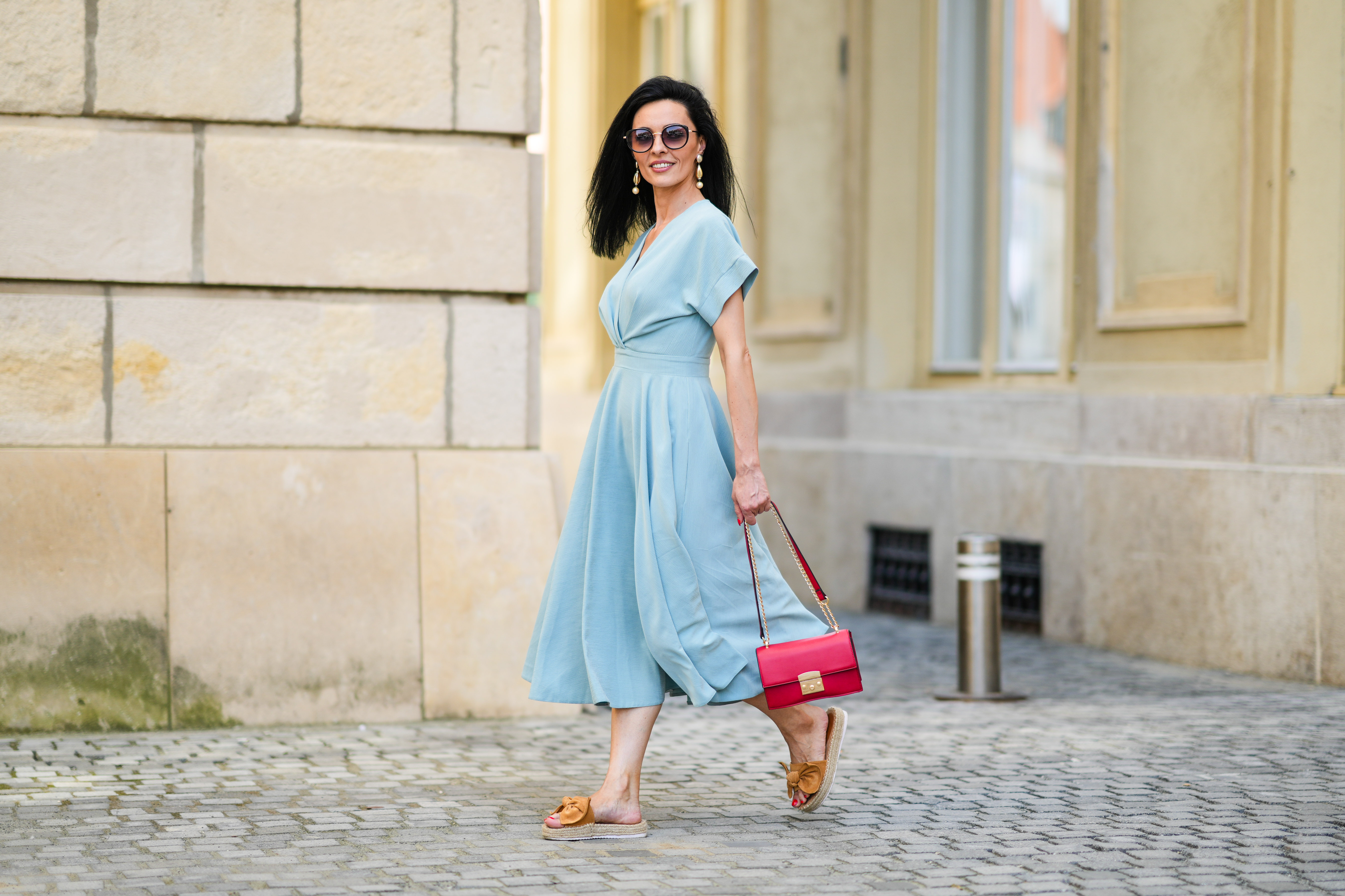 SIBIU, ROMANIA - JULY 27: Cosmina Pasarin wears sunglasses, a pastel blue gathered low-neck midi dress, a red bag, brown sandals with platform beige wicker platforms, on July 27, 2021 in Sibiu, Romania. (Photo by Edward Berthelot/Getty Images)
