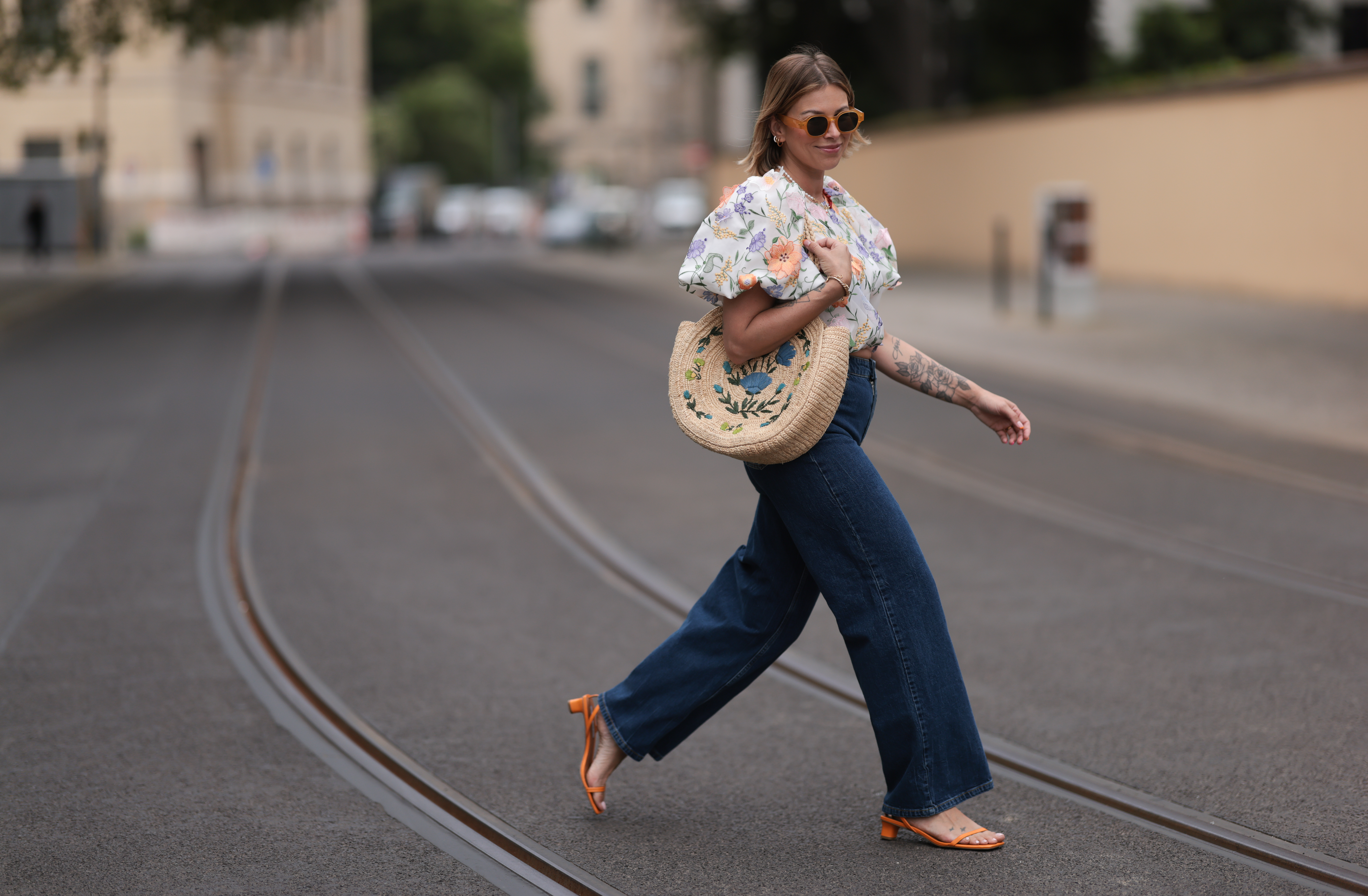 Aline Kaplan wearing Baum & Pferdgarten wide leg blue denim pants, & other stories white flower pattern cropped blouse and orange summer heels and Mango orange black shades on June 06, 2023 in Berlin, Germany.